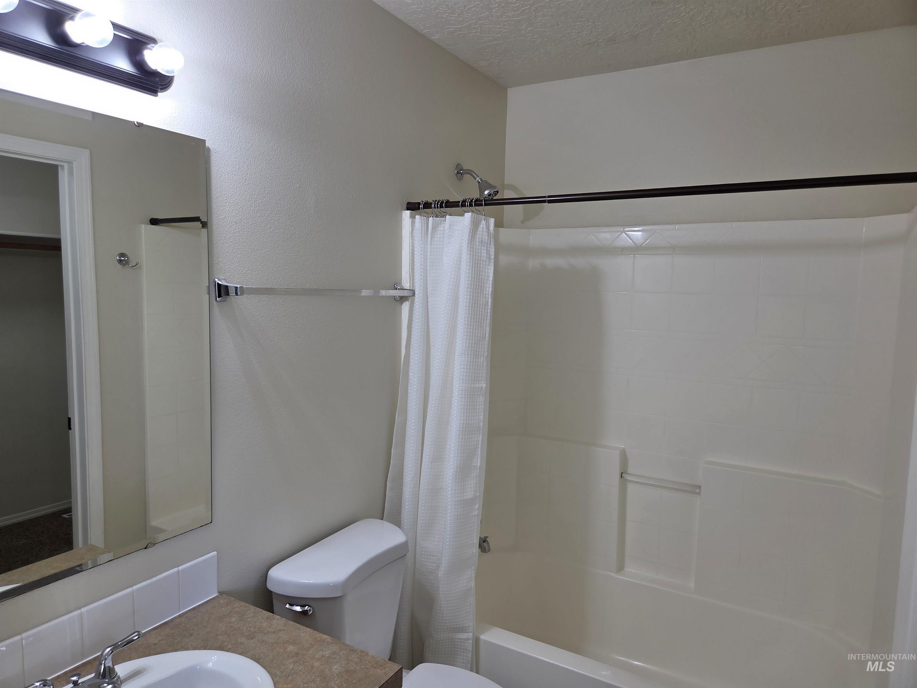 Bathroom featuring shower / bathtub combination with curtain, a textured ceiling, and vanity