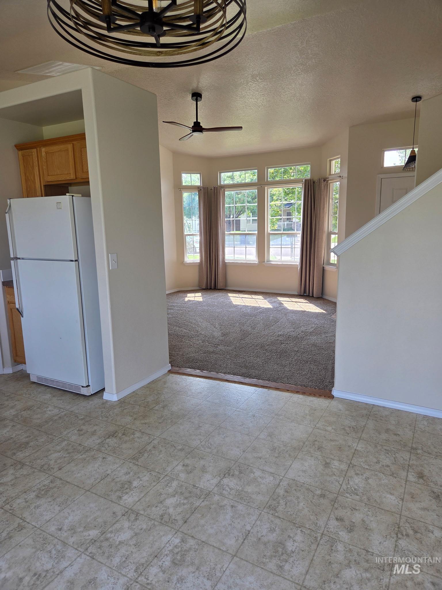 Unfurnished living room featuring a textured ceiling, a ceiling fan, and light colored carpet