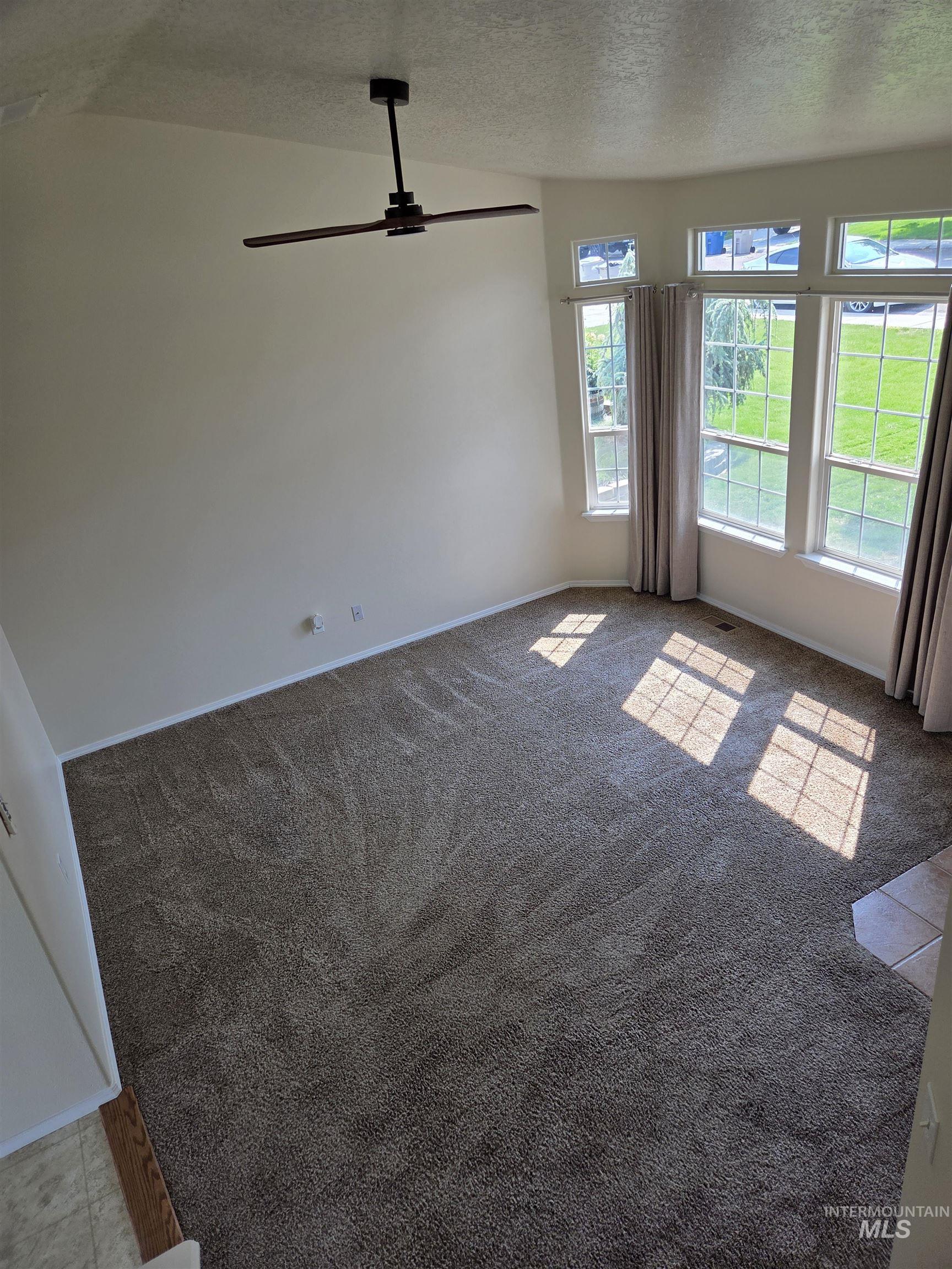 Unfurnished living room with a textured ceiling, light colored carpet, and a ceiling fan