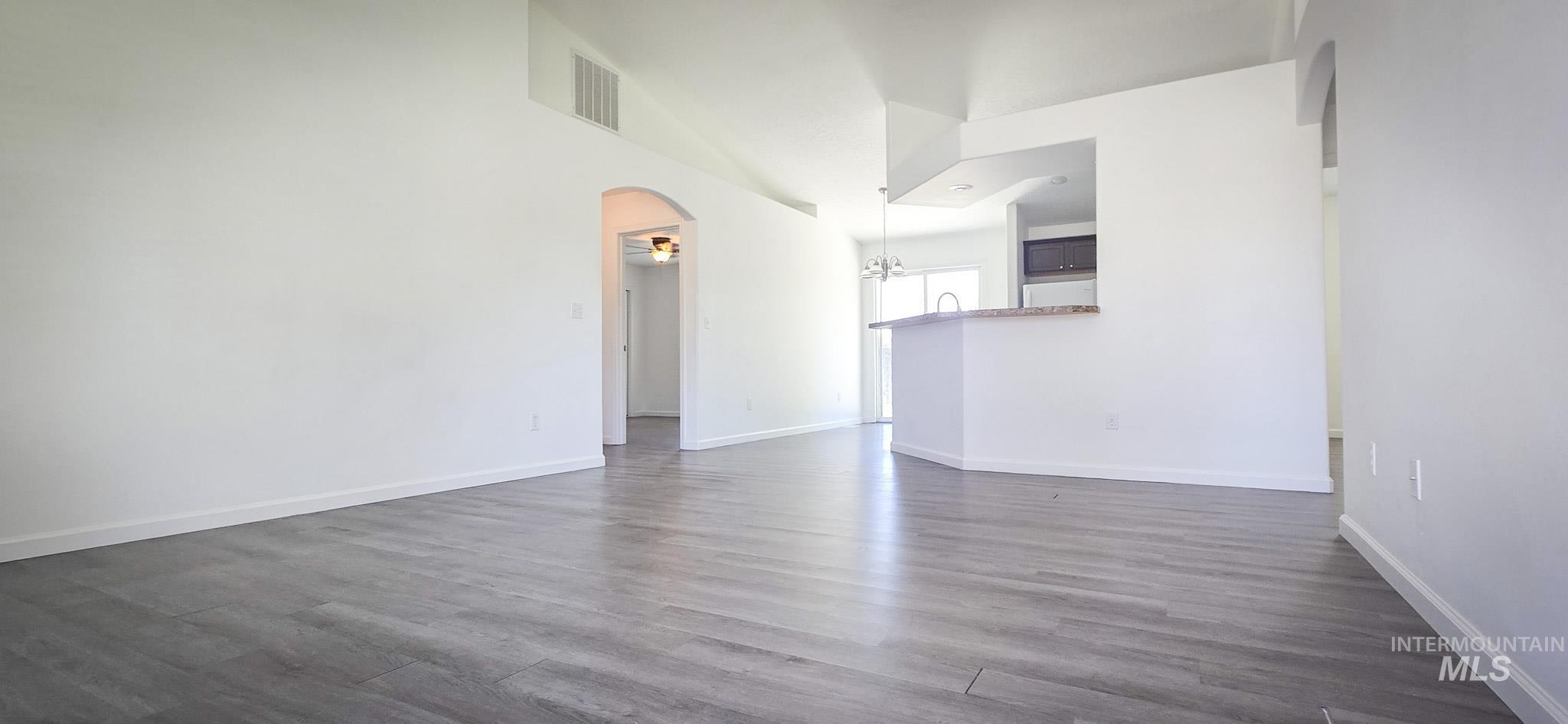Unfurnished living room with arched walkways and dark wood-style floors