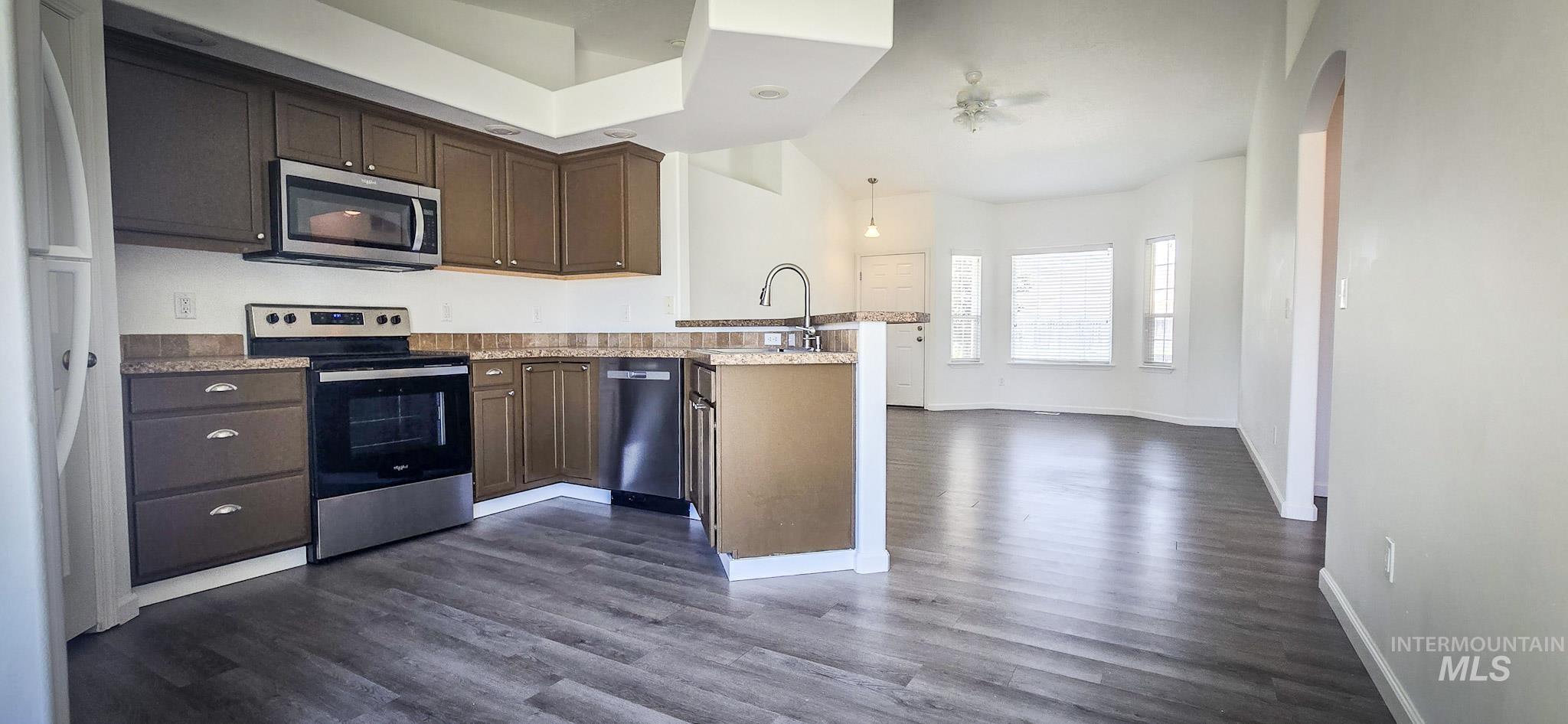 Kitchen featuring a peninsula, appliances with stainless steel finishes, dark wood finished floors, light countertops, and dark brown cabinets