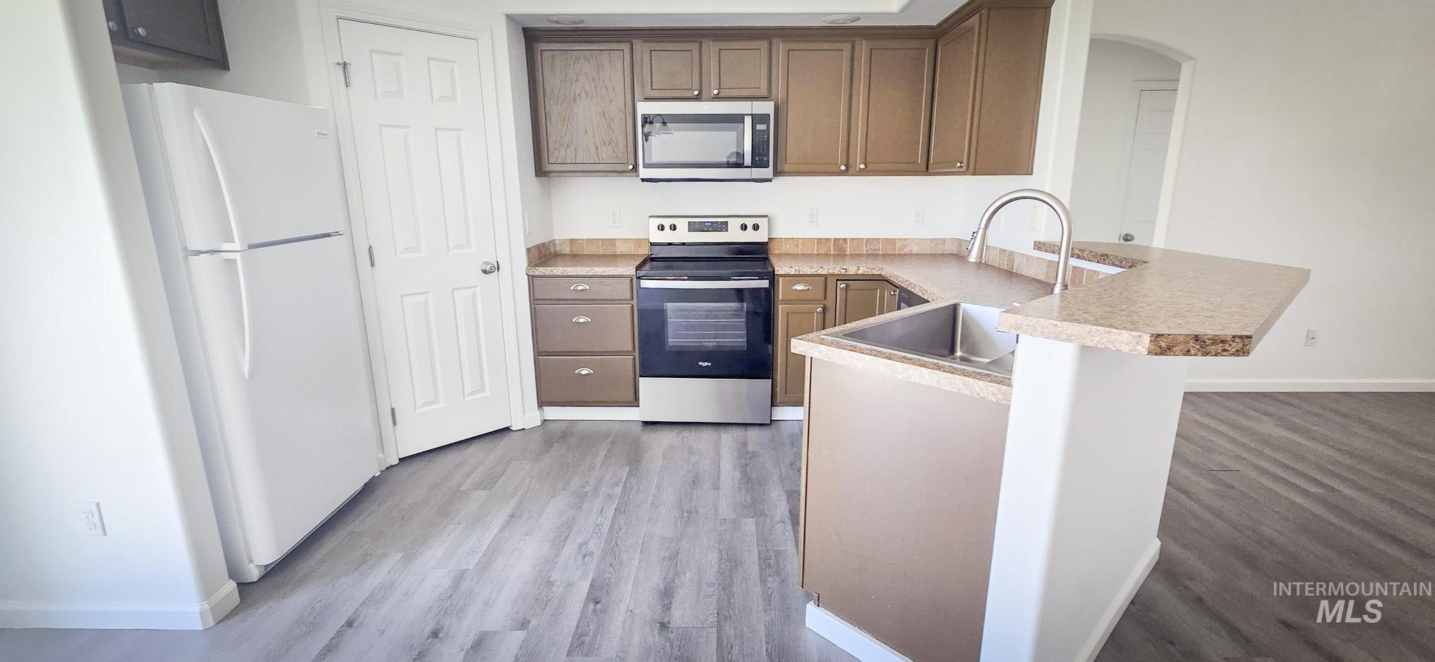 Kitchen featuring a peninsula, appliances with stainless steel finishes, a kitchen bar, light countertops, and light wood-style floors