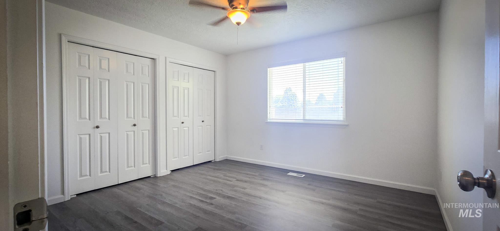 Unfurnished bedroom with multiple closets, dark wood-type flooring, a ceiling fan, and a textured ceiling