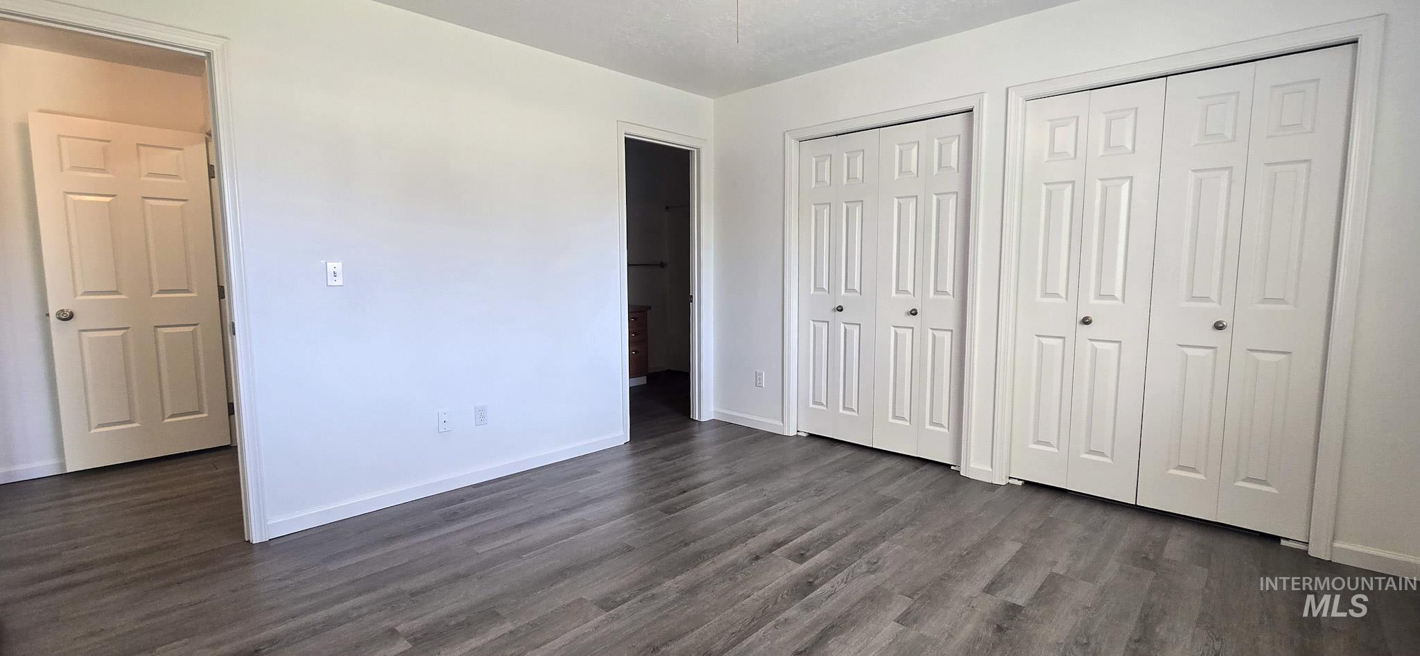 Unfurnished bedroom featuring multiple closets and dark wood finished floors