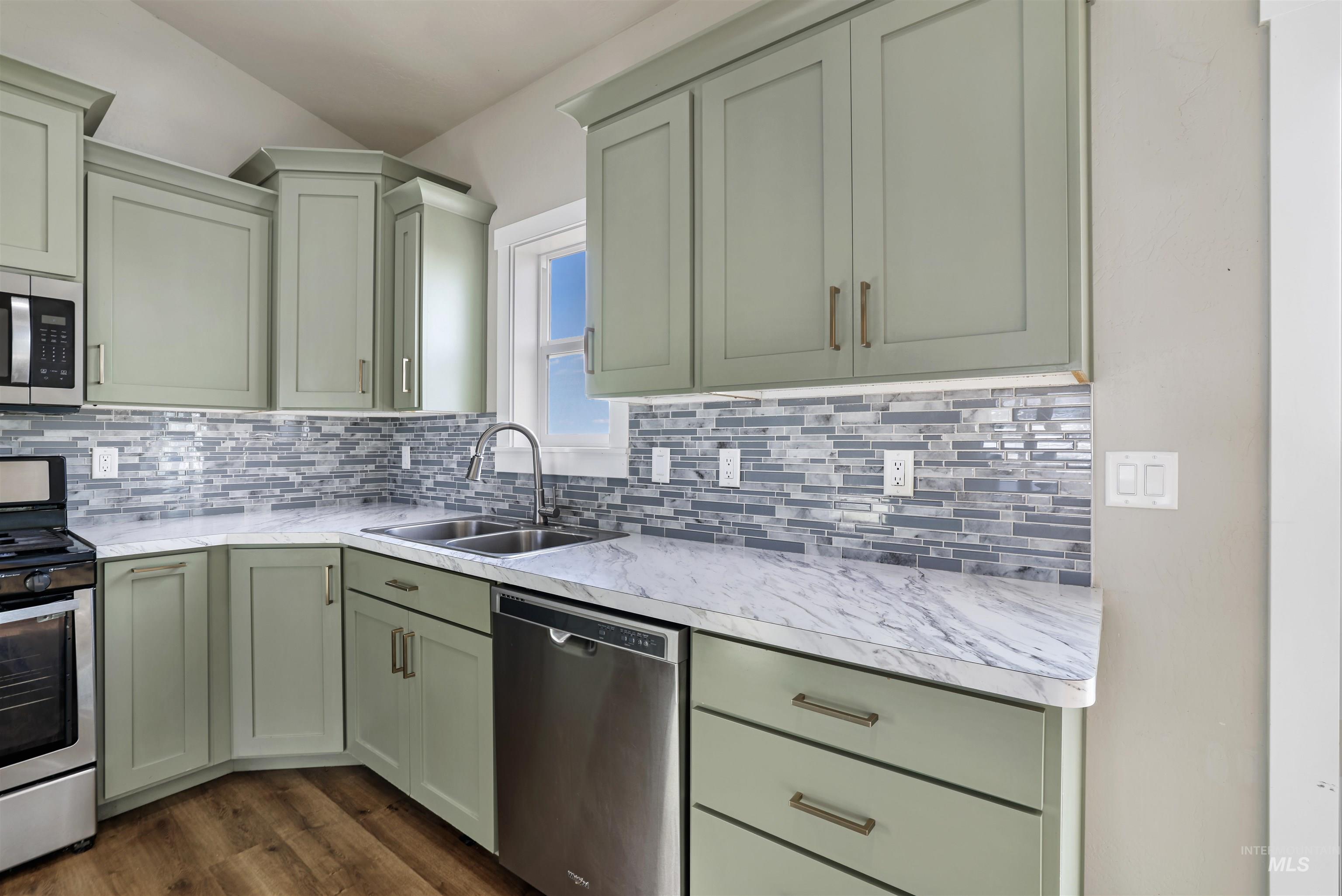 Kitchen with green cabinetry, stainless steel appliances, tasteful backsplash, and dark wood-type flooring