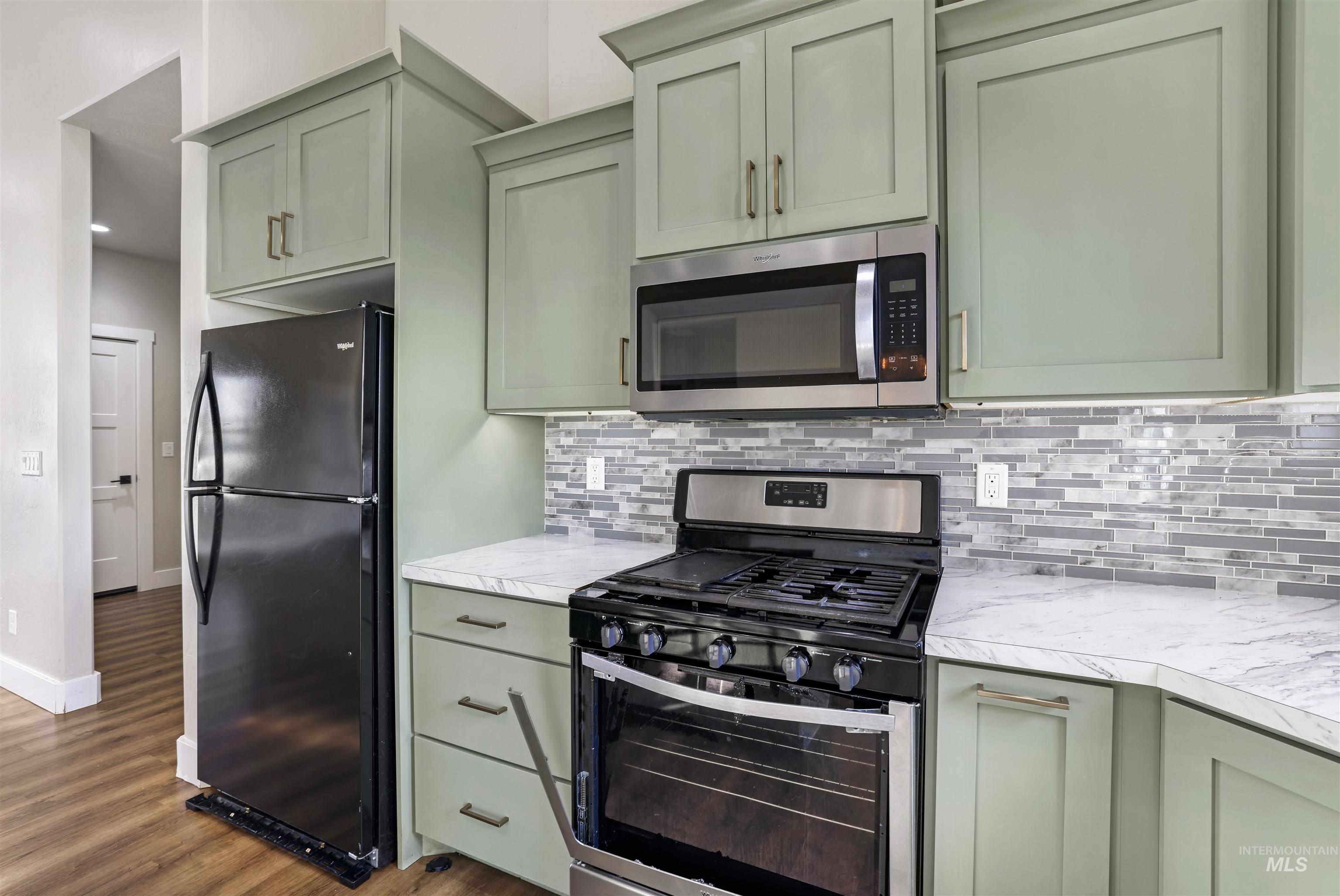 Kitchen featuring appliances with stainless steel finishes, light countertops, dark wood-style flooring, decorative backsplash, and green cabinets