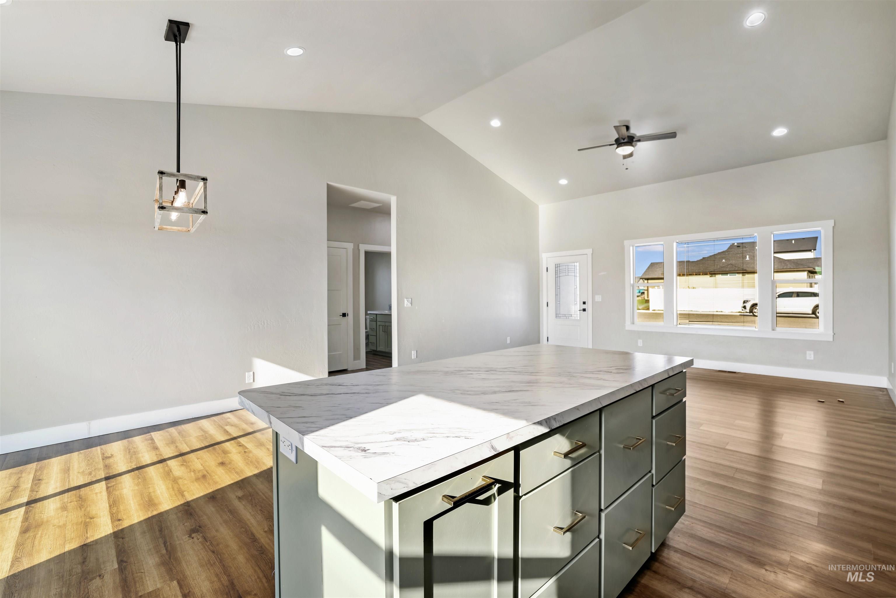 Kitchen with a kitchen island, vaulted ceiling, light countertops, dark wood-style floors, and pendant lighting