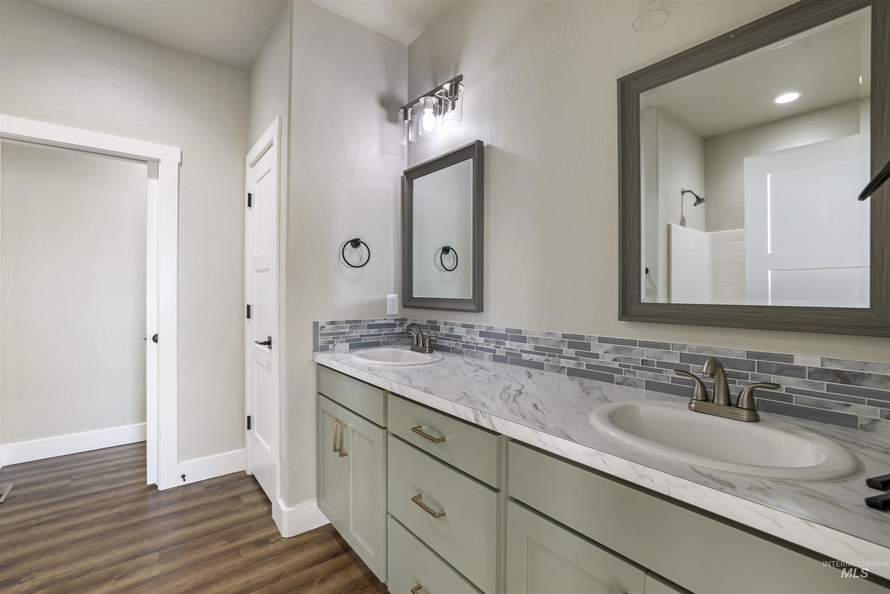 Bathroom featuring double vanity, dark wood-style flooring, tasteful backsplash, a shower, and recessed lighting