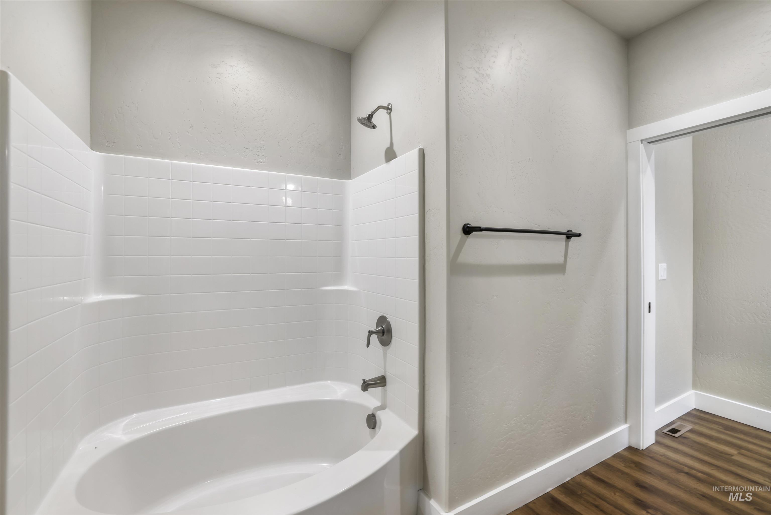 Full bathroom with a textured wall, shower / washtub combination, and dark wood finished floors