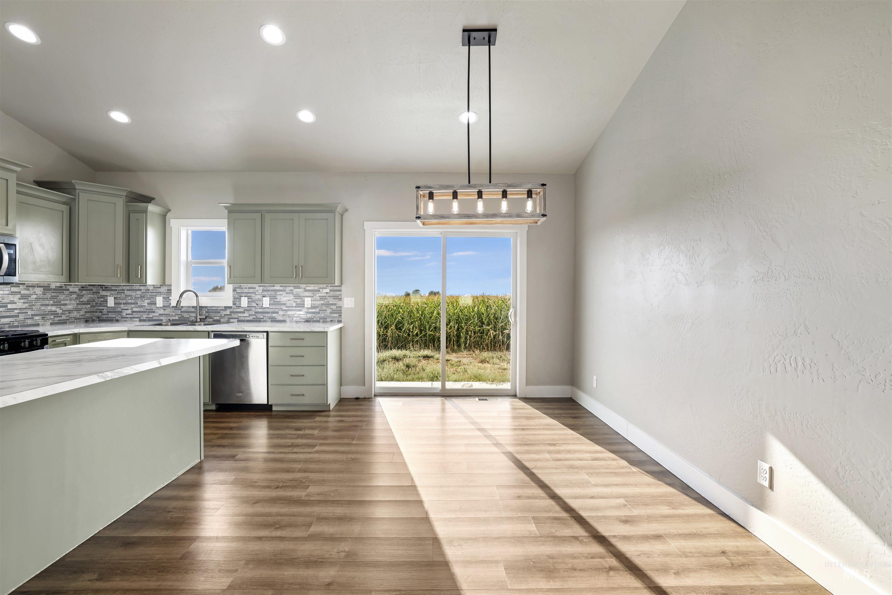Kitchen with tasteful backsplash, hanging light fixtures, stainless steel appliances, dark wood finished floors, and green cabinets
