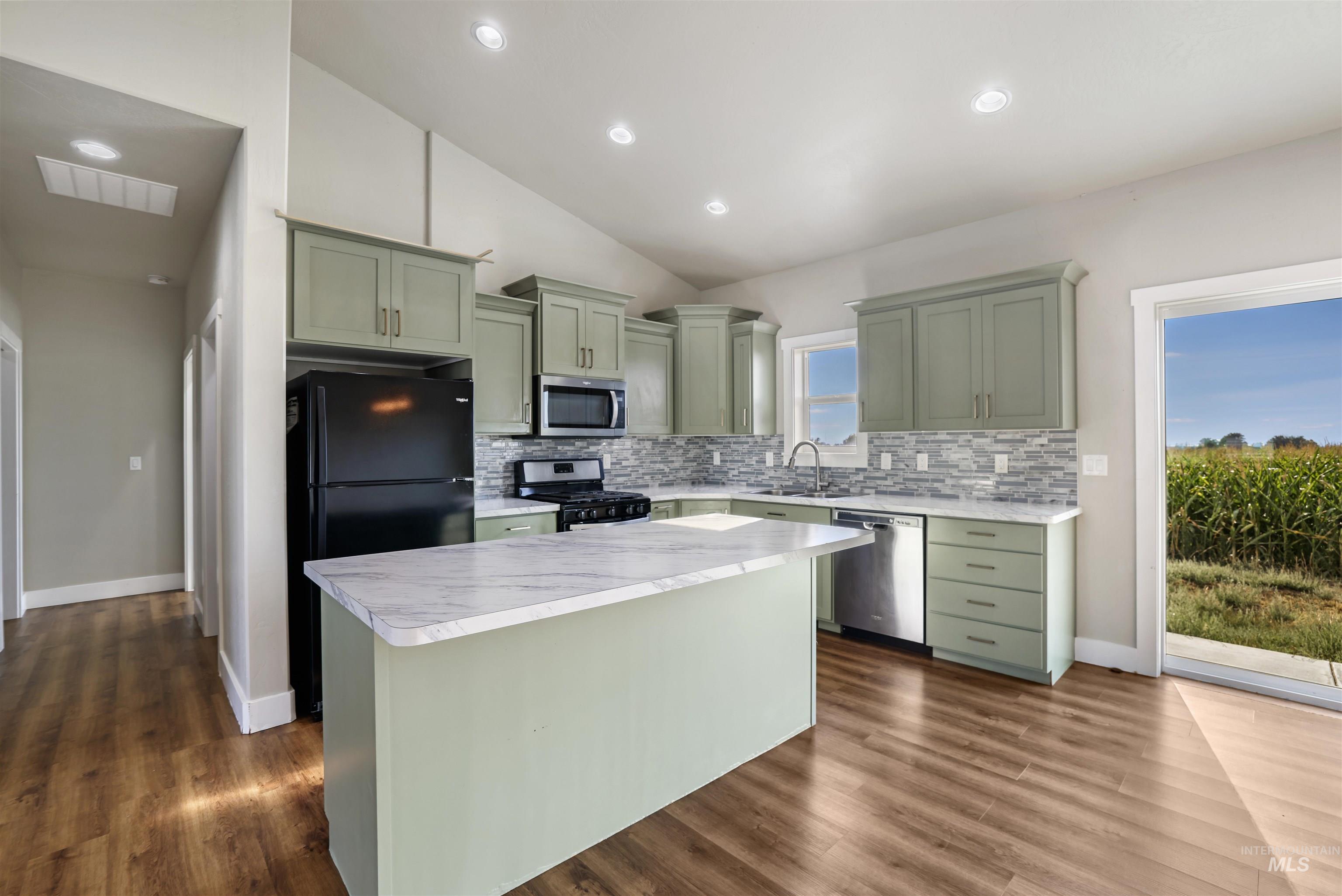 Kitchen with green cabinetry, light countertops, lofted ceiling, appliances with stainless steel finishes, and a kitchen island