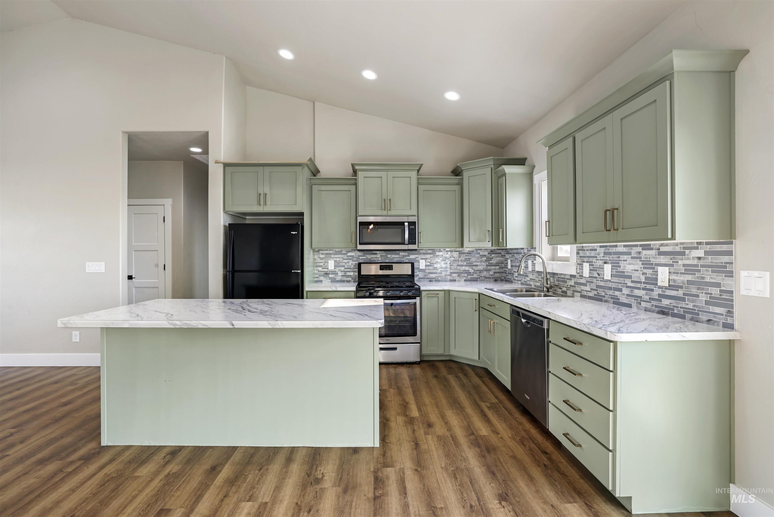 Kitchen with green cabinetry, vaulted ceiling, appliances with stainless steel finishes, a center island, and dark wood-style flooring