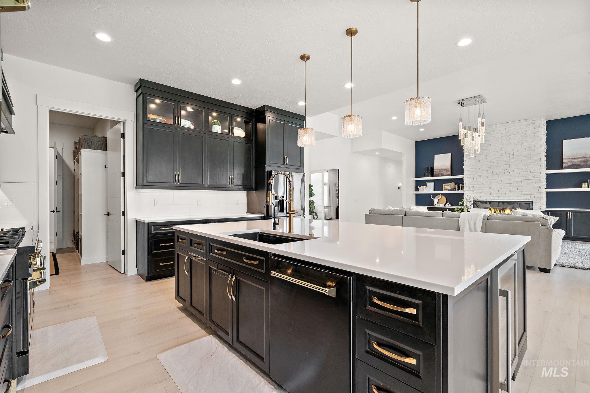 Kitchen with dark cabinets, dishwasher, a fireplace, glass insert cabinets, and hanging light fixtures