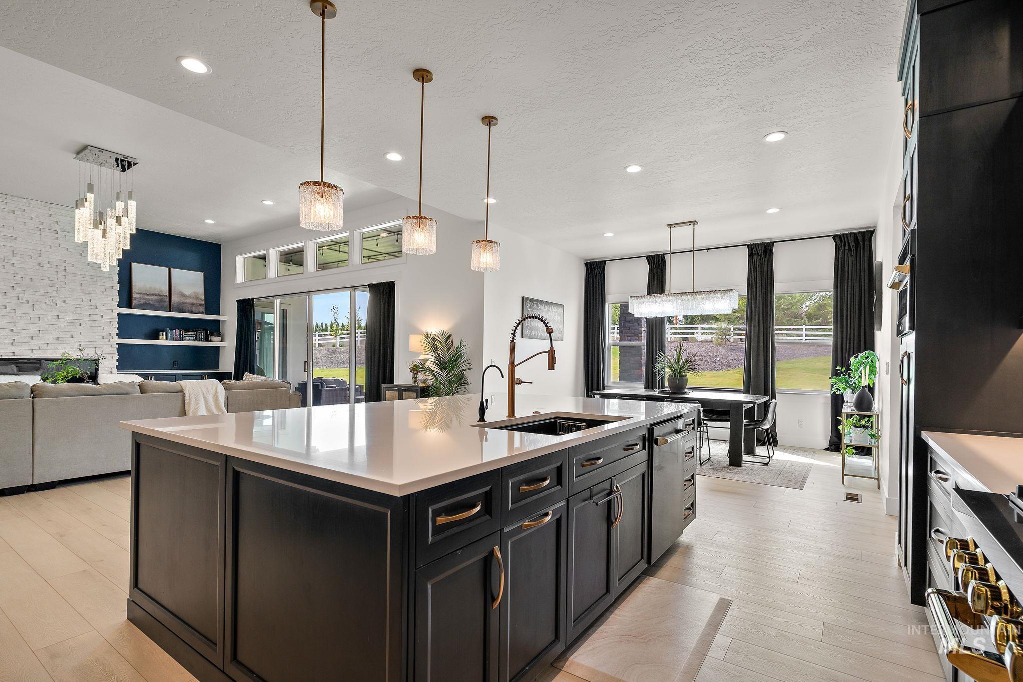 Kitchen with dark cabinetry, pendant lighting, open floor plan, a center island with sink, and light wood finished floors