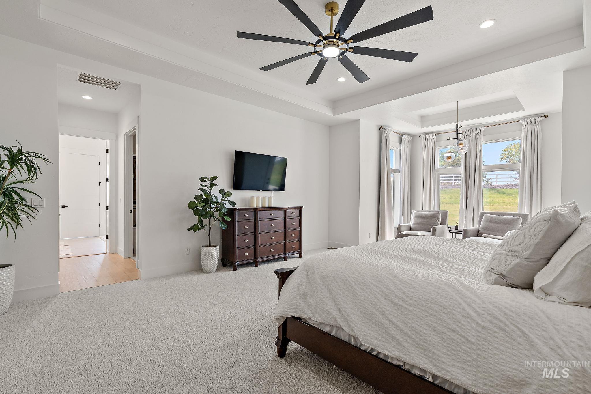 Carpeted bedroom with a raised ceiling, recessed lighting, and ceiling fan
