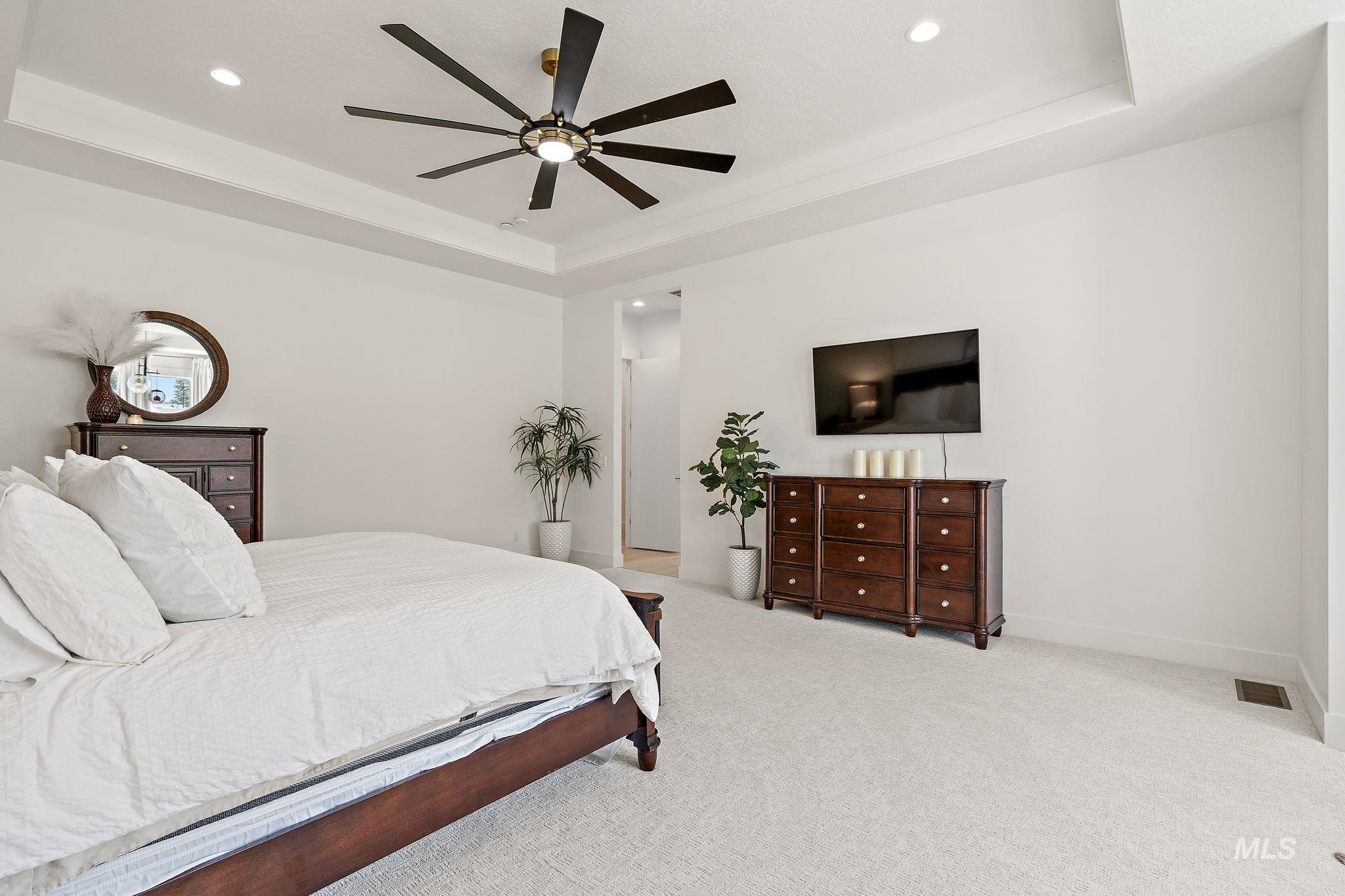 Carpeted bedroom with a raised ceiling, ceiling fan, and recessed lighting