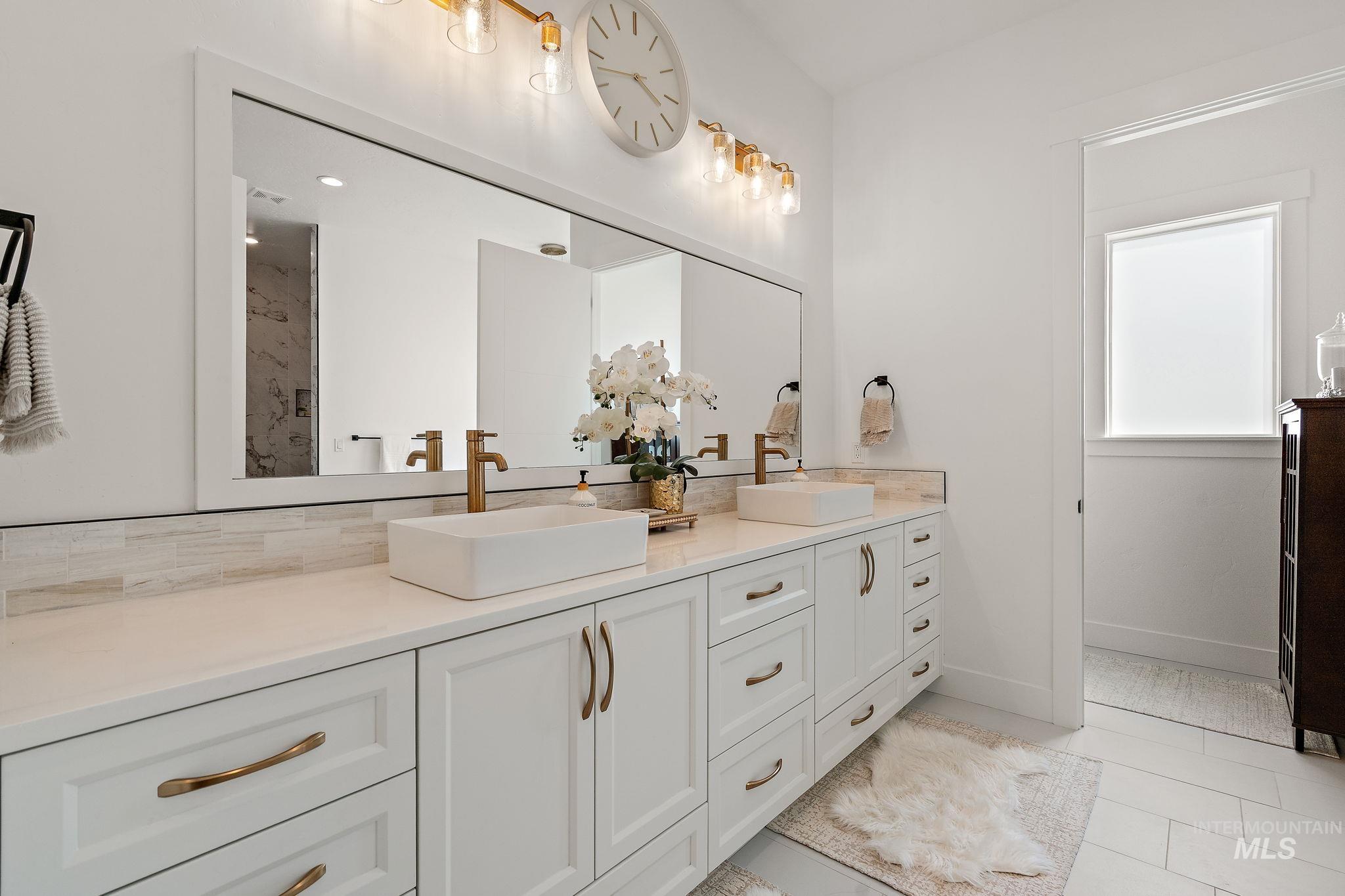 Bathroom with double vanity, light tile patterned flooring, a marble finish shower, and backsplash