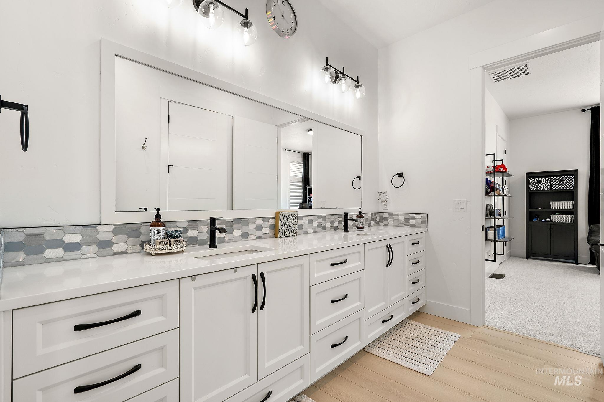 Bathroom with double vanity, tasteful backsplash, and light wood finished floors