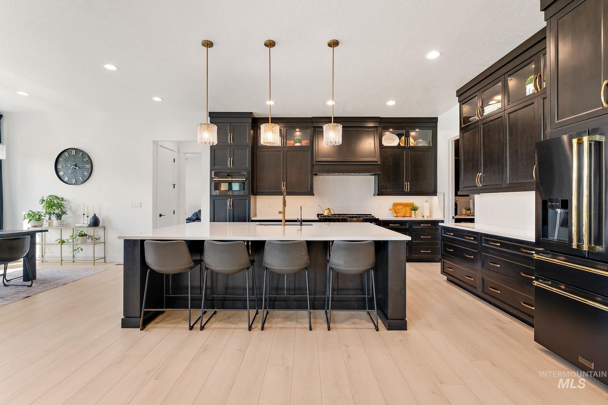Kitchen featuring a breakfast bar, recessed lighting, hanging light fixtures, high end black fridge, and glass insert cabinets