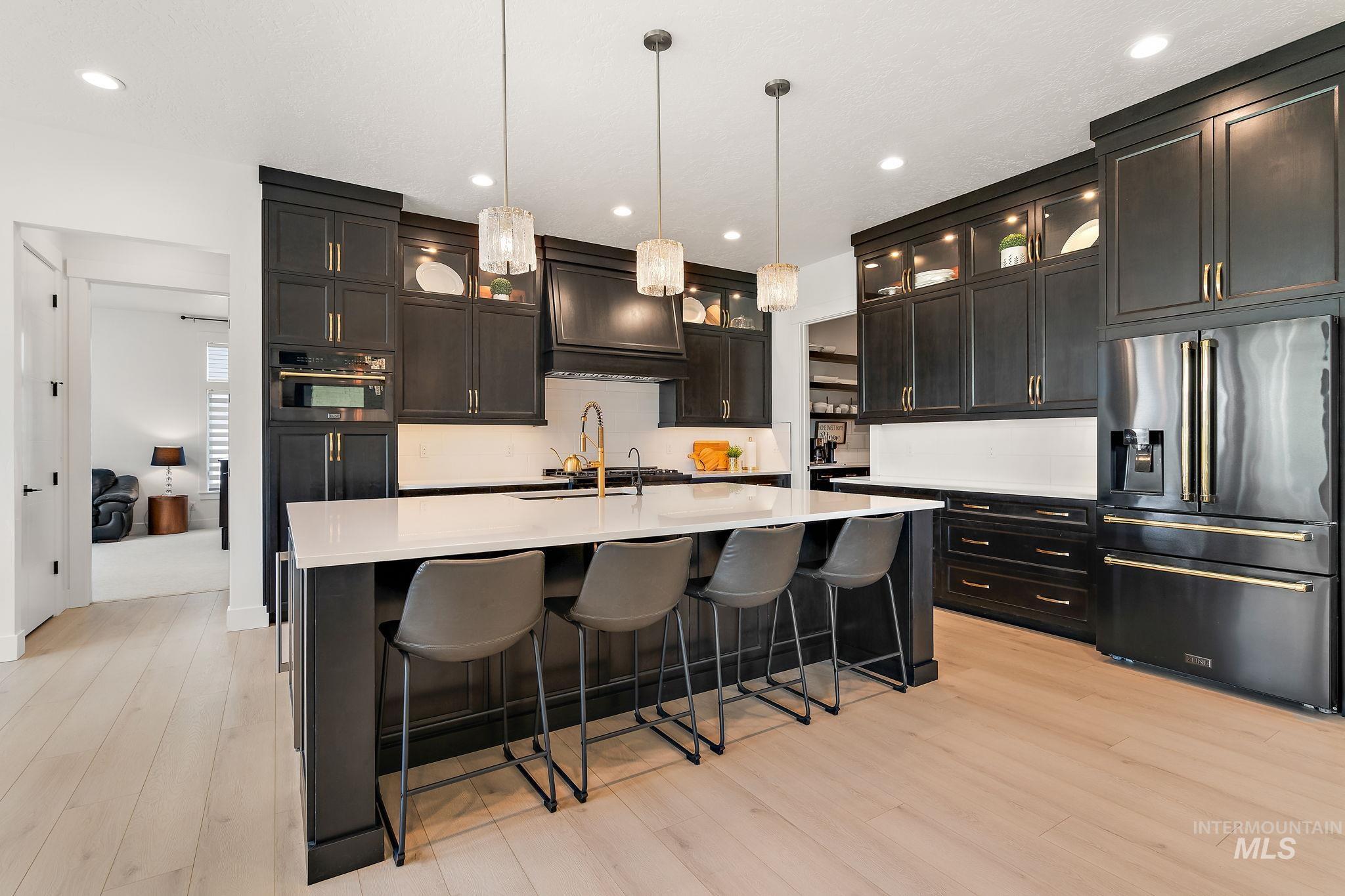 Kitchen featuring a breakfast bar, high end fridge, decorative light fixtures, glass insert cabinets, and light wood finished floors