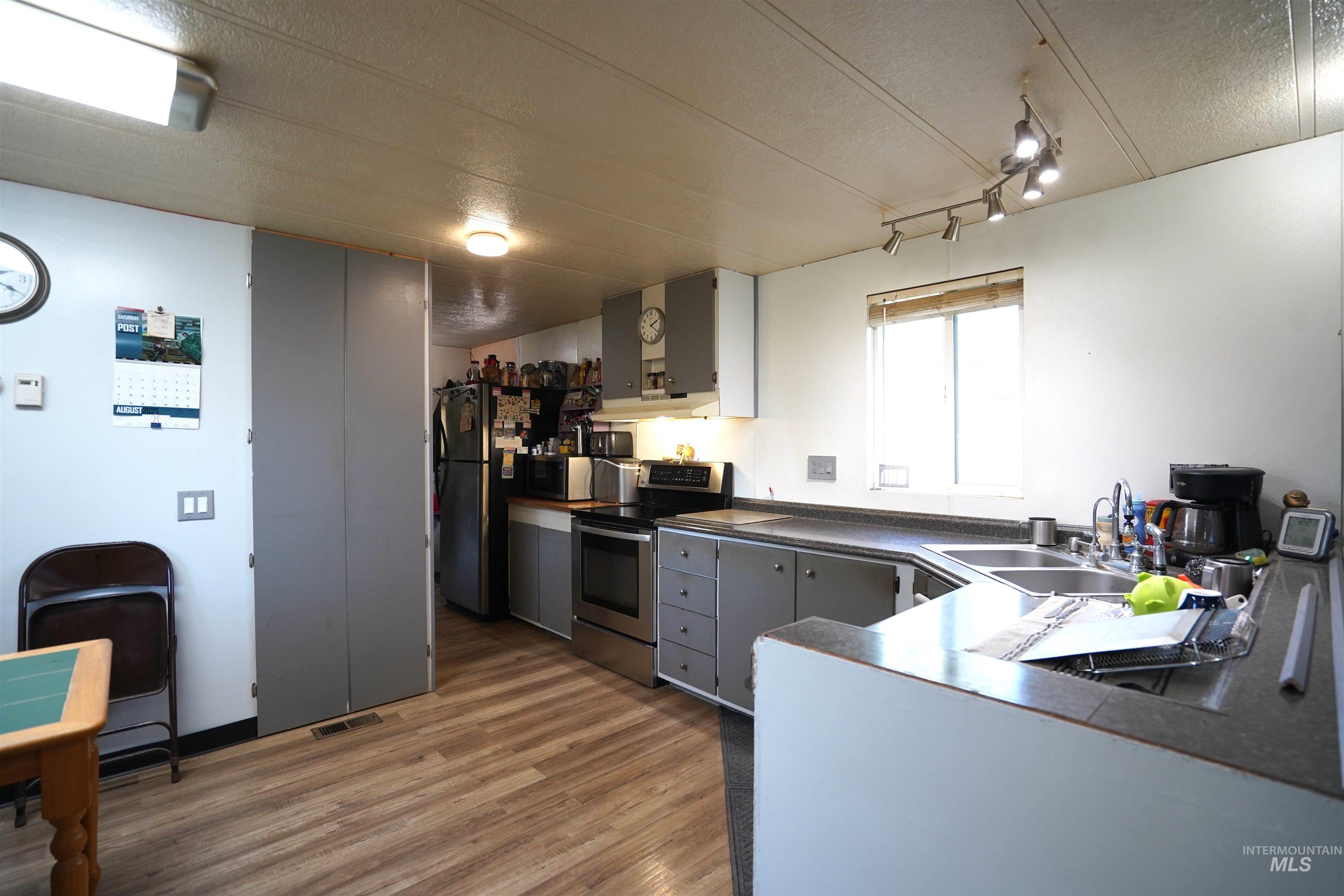 Kitchen with dark countertops, a textured ceiling, stainless steel appliances, gray cabinetry, and light wood-style flooring