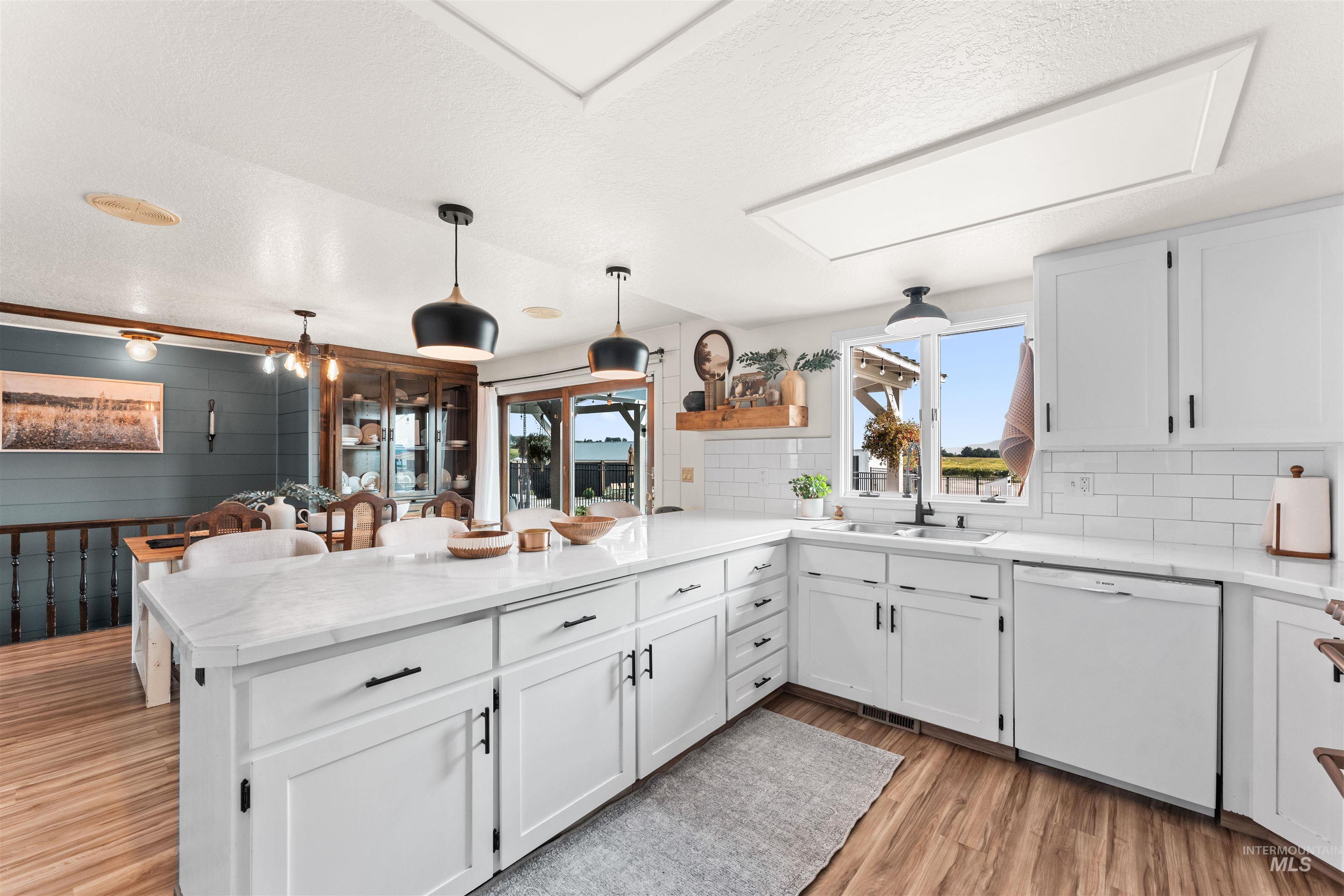 Kitchen with a peninsula, light wood-type flooring, white dishwasher, white cabinetry, and pendant lighting