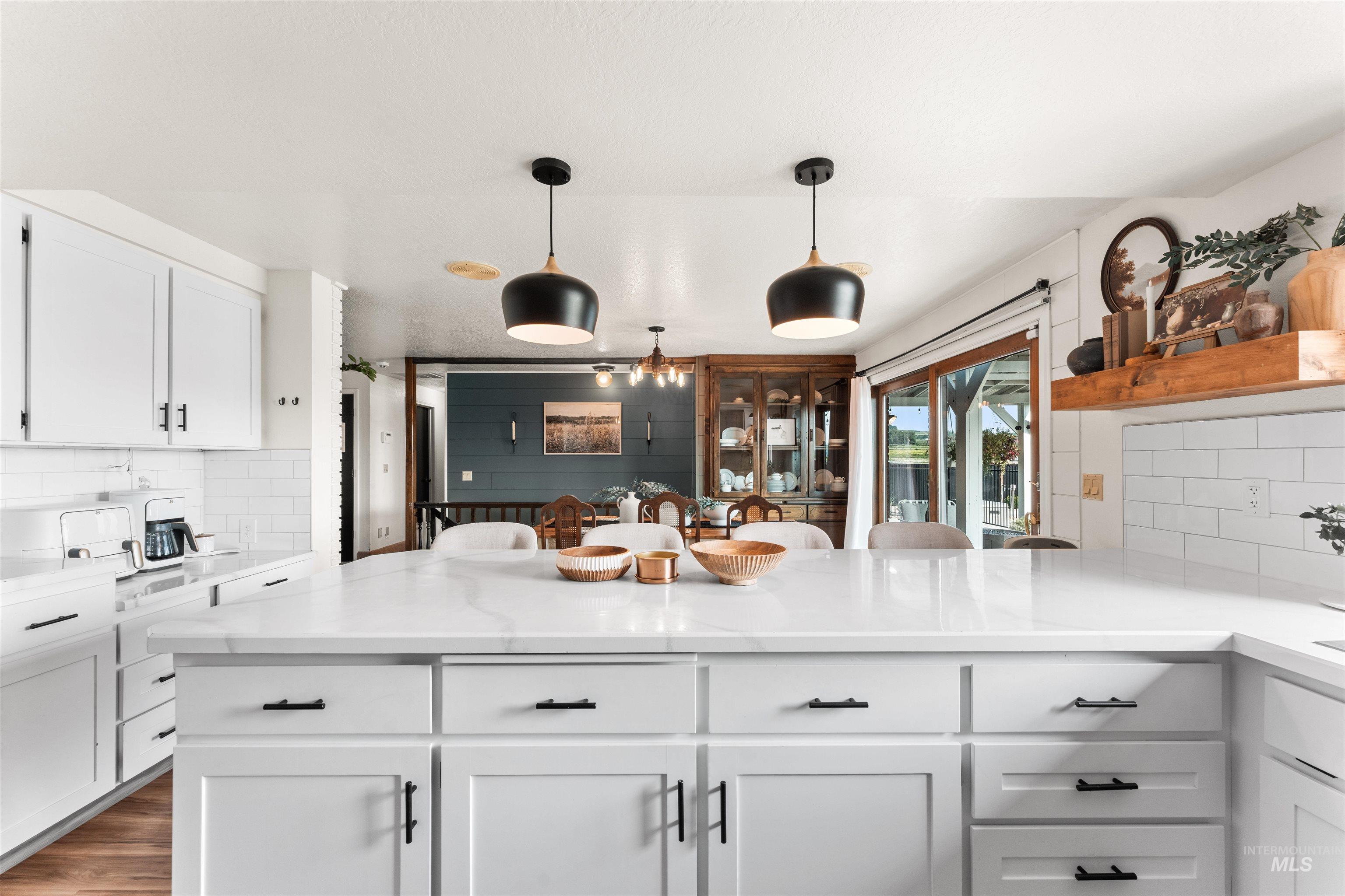 Kitchen featuring tasteful backsplash, white cabinets, pendant lighting, a peninsula, and light stone countertops
