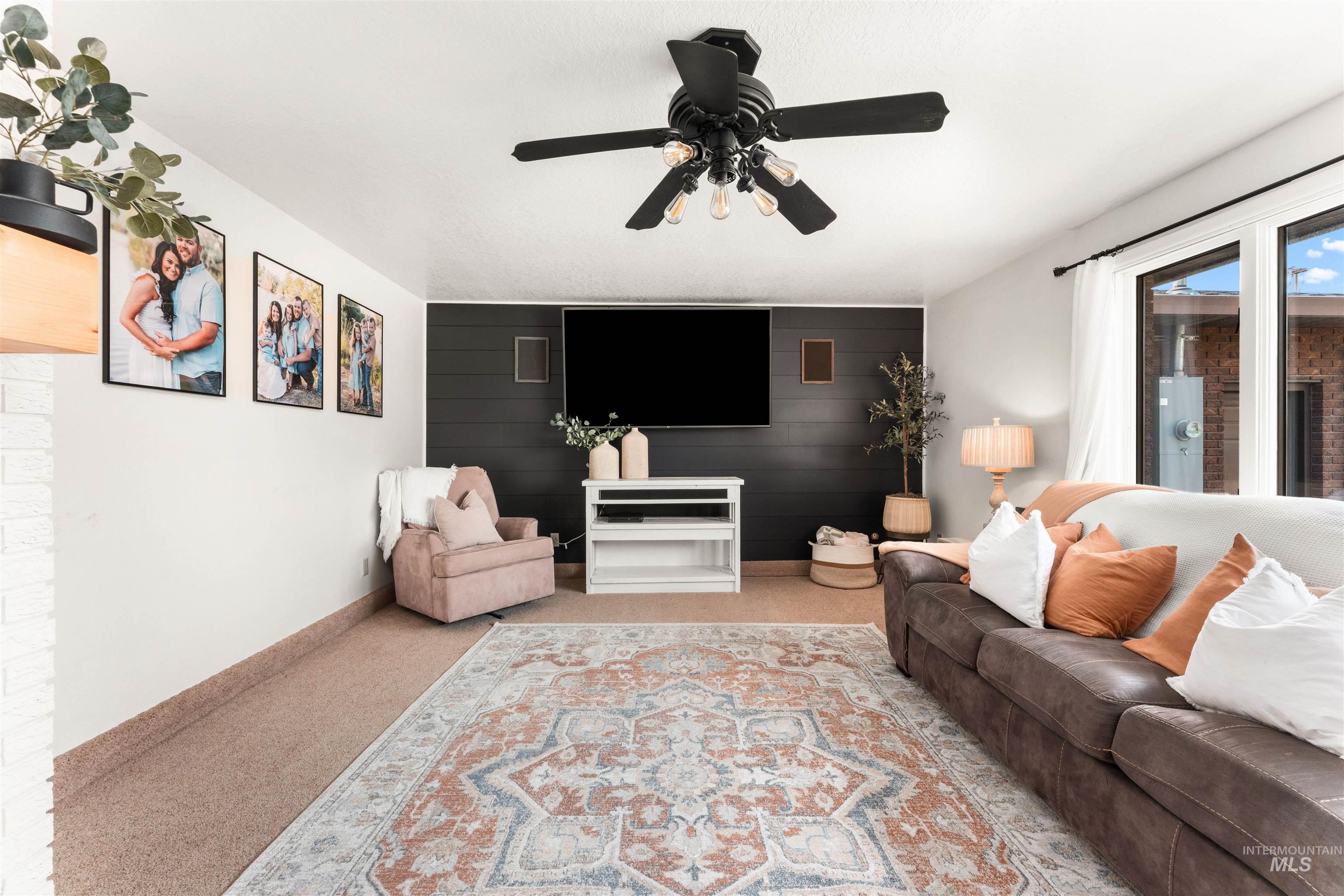 Carpeted living area featuring ceiling fan, wood walls, and an accent wall