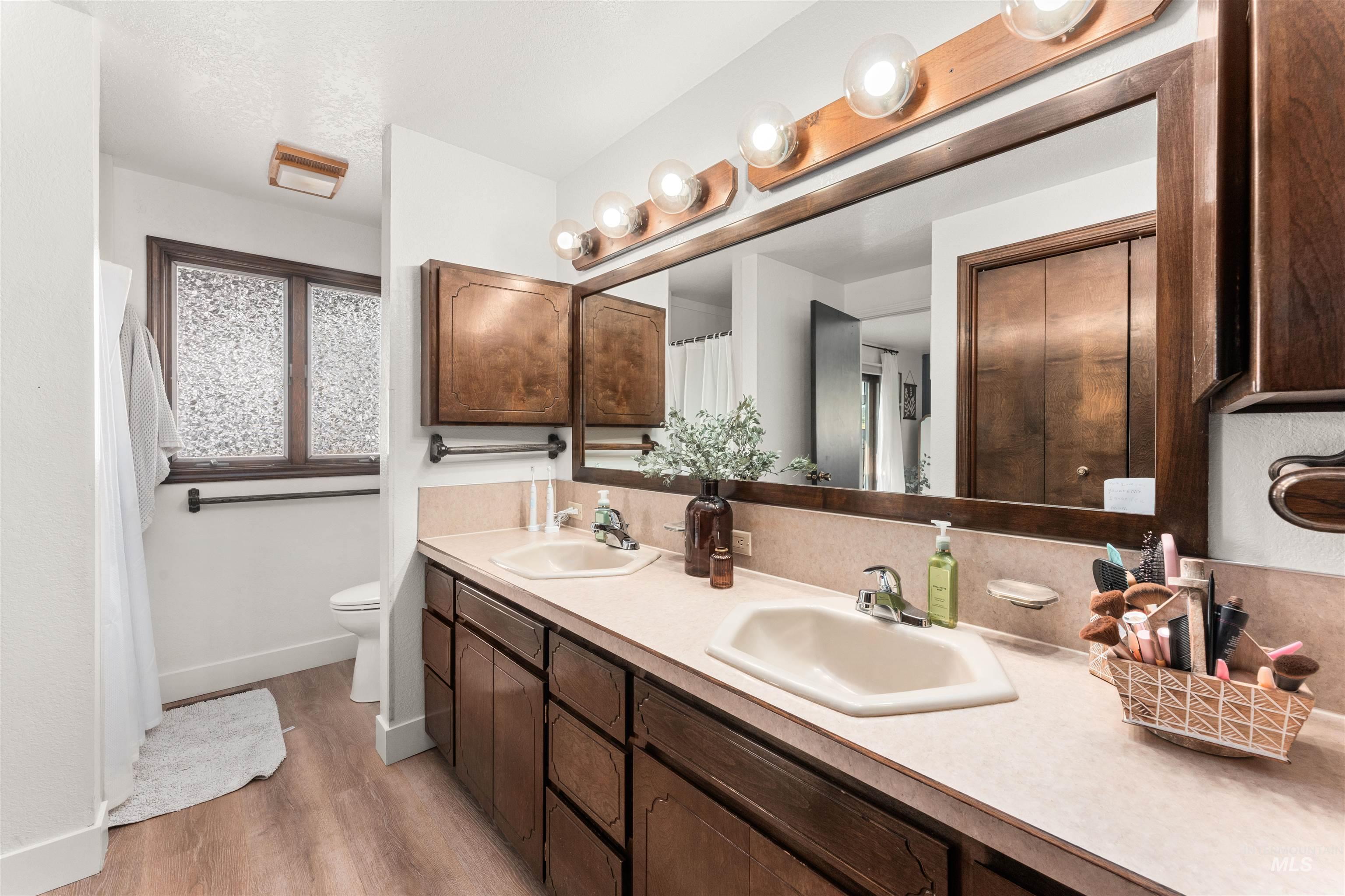 Bathroom with double vanity, light wood finished floors, and a textured ceiling