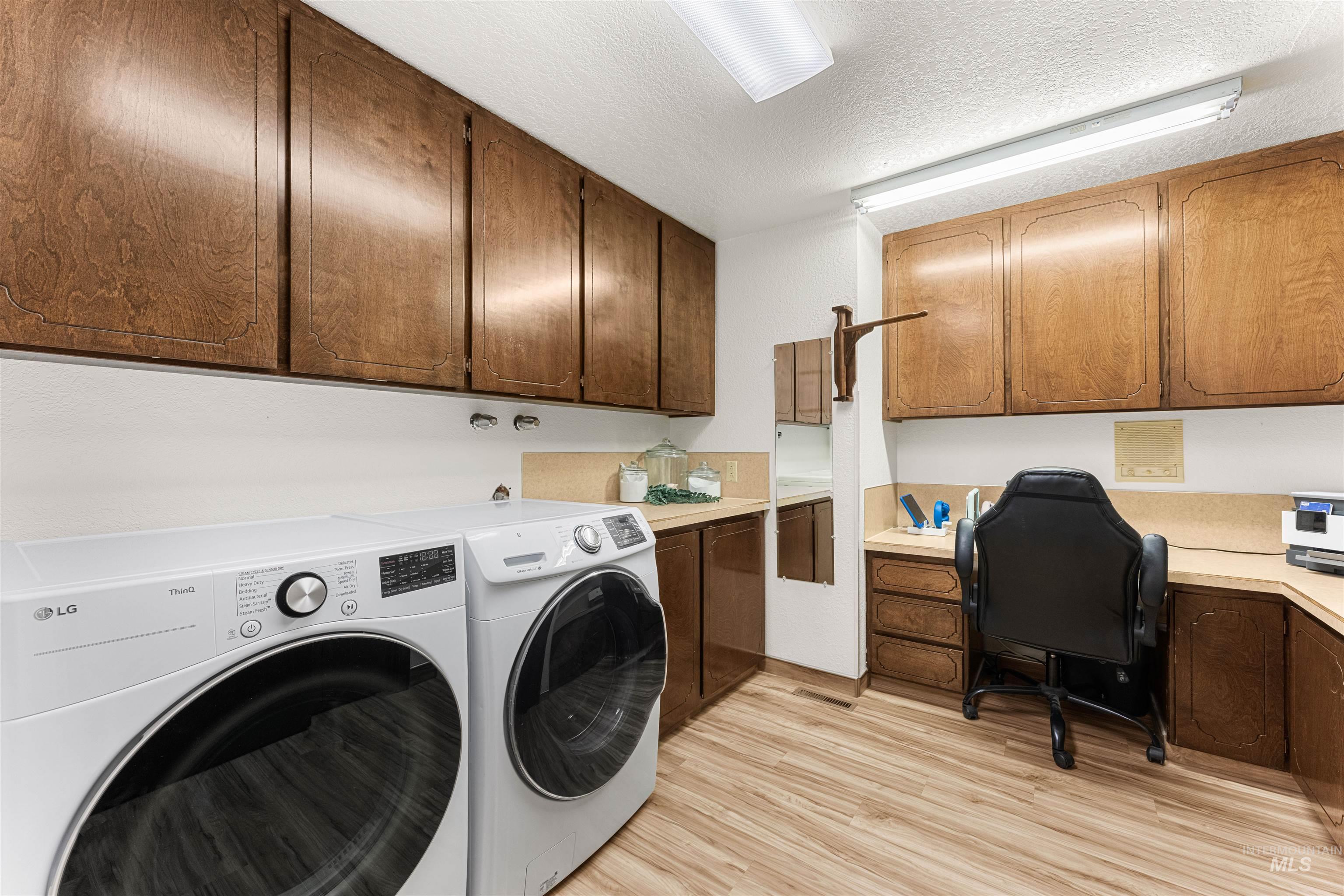 Laundry area featuring light wood-type flooring, a textured ceiling, an office area, independent washer and dryer, and cabinet space