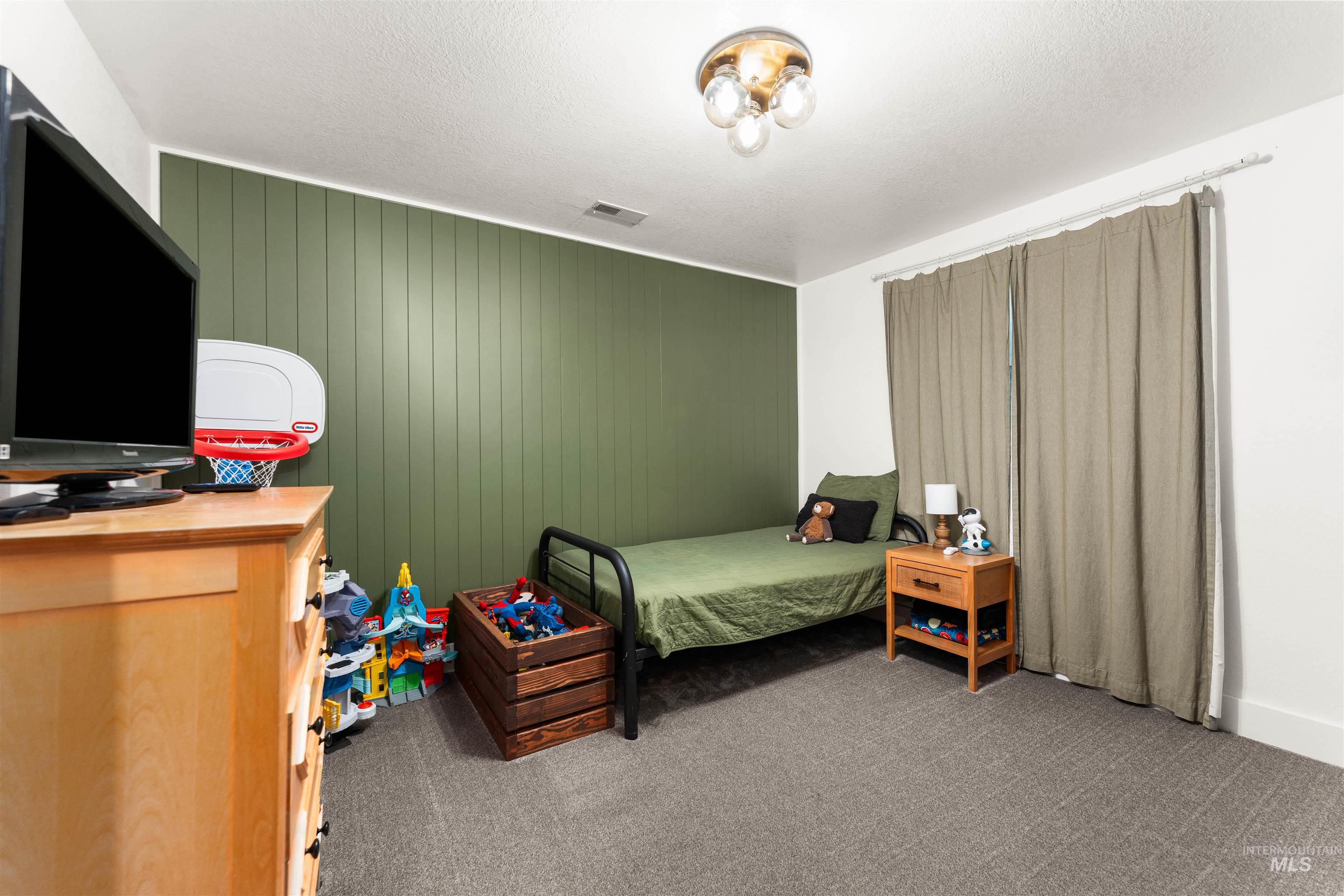 Carpeted bedroom featuring a textured ceiling and wooden walls