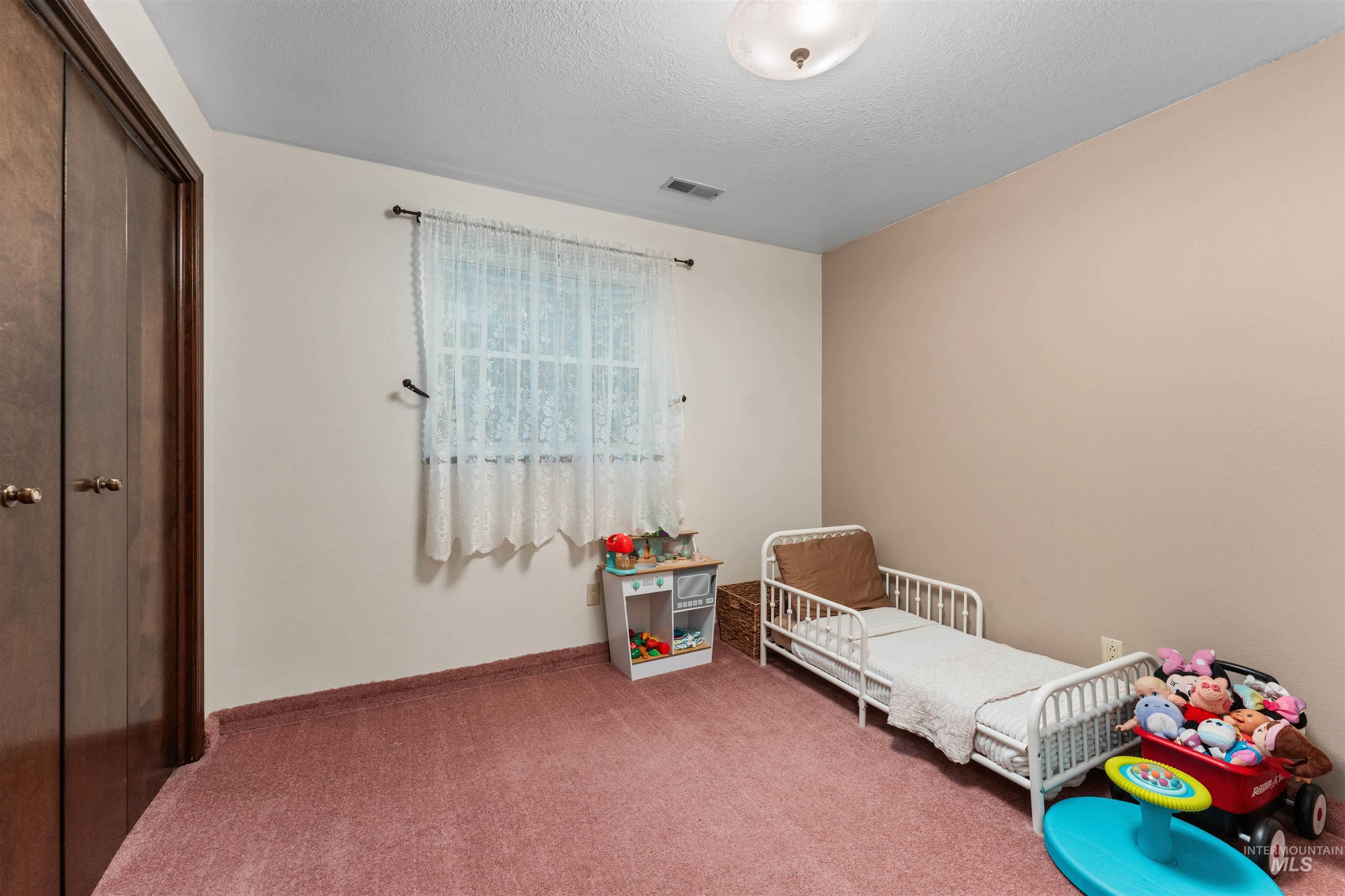 Bedroom with carpet, a textured ceiling, a nursery area, and a closet