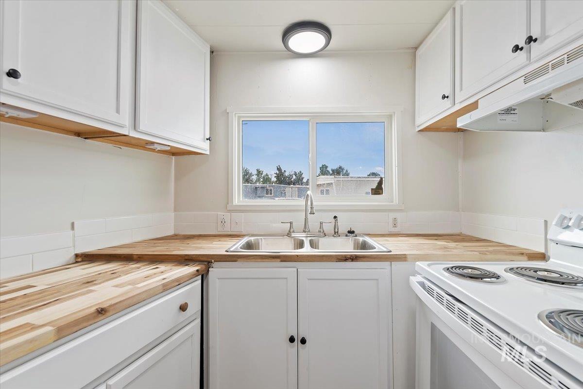 Kitchen featuring wood counters, white cabinetry, white electric stove, and under cabinet range hood