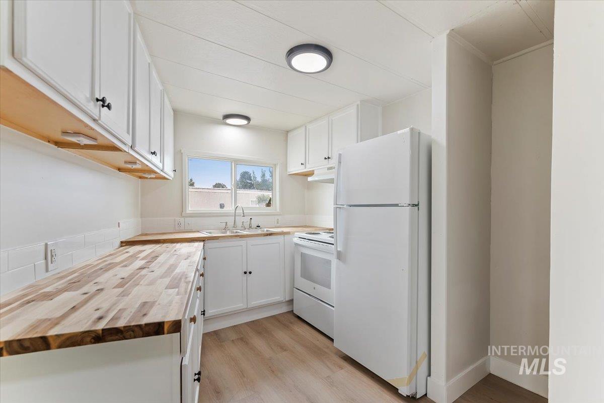 Kitchen with butcher block countertops, white cabinetry, white appliances, light wood finished floors, and under cabinet range hood