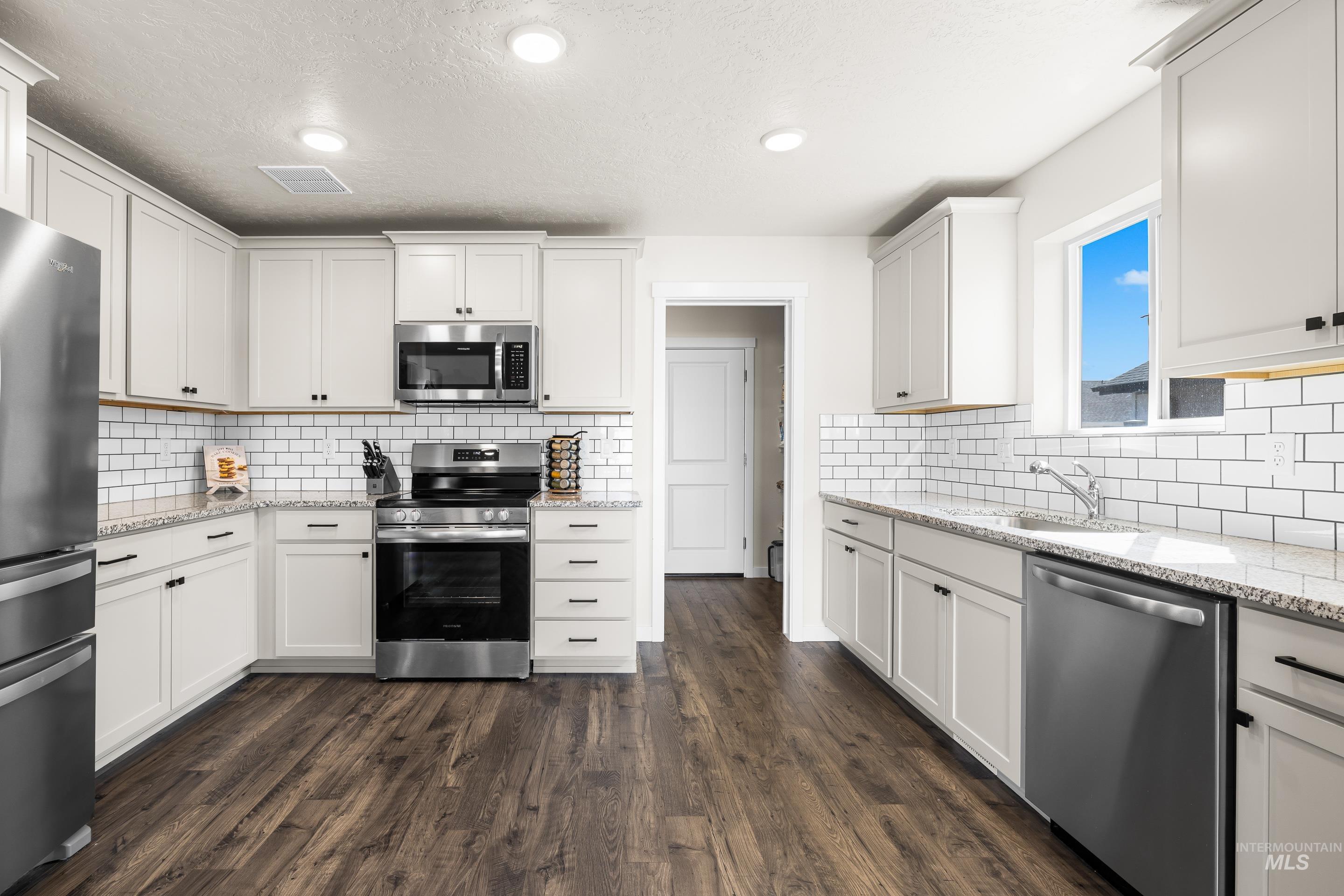Kitchen featuring light stone counters, white cabinetry, appliances with stainless steel finishes, recessed lighting, and tasteful backsplash