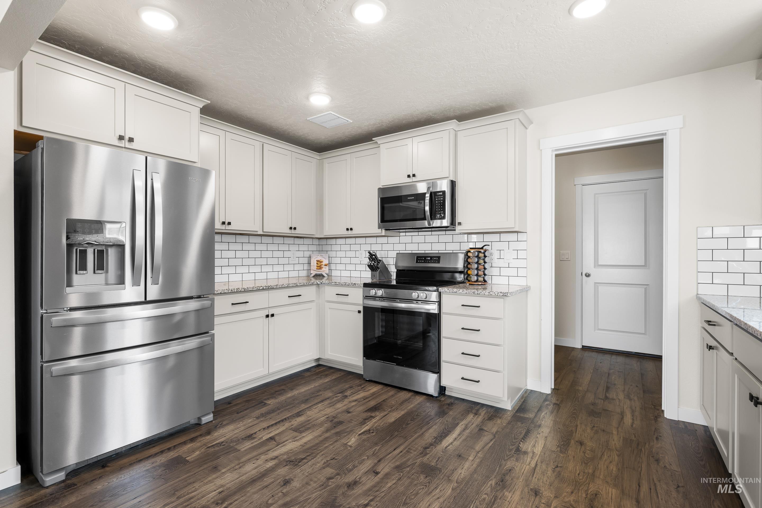 Kitchen with stainless steel appliances, white cabinets, backsplash, light stone counters, and recessed lighting