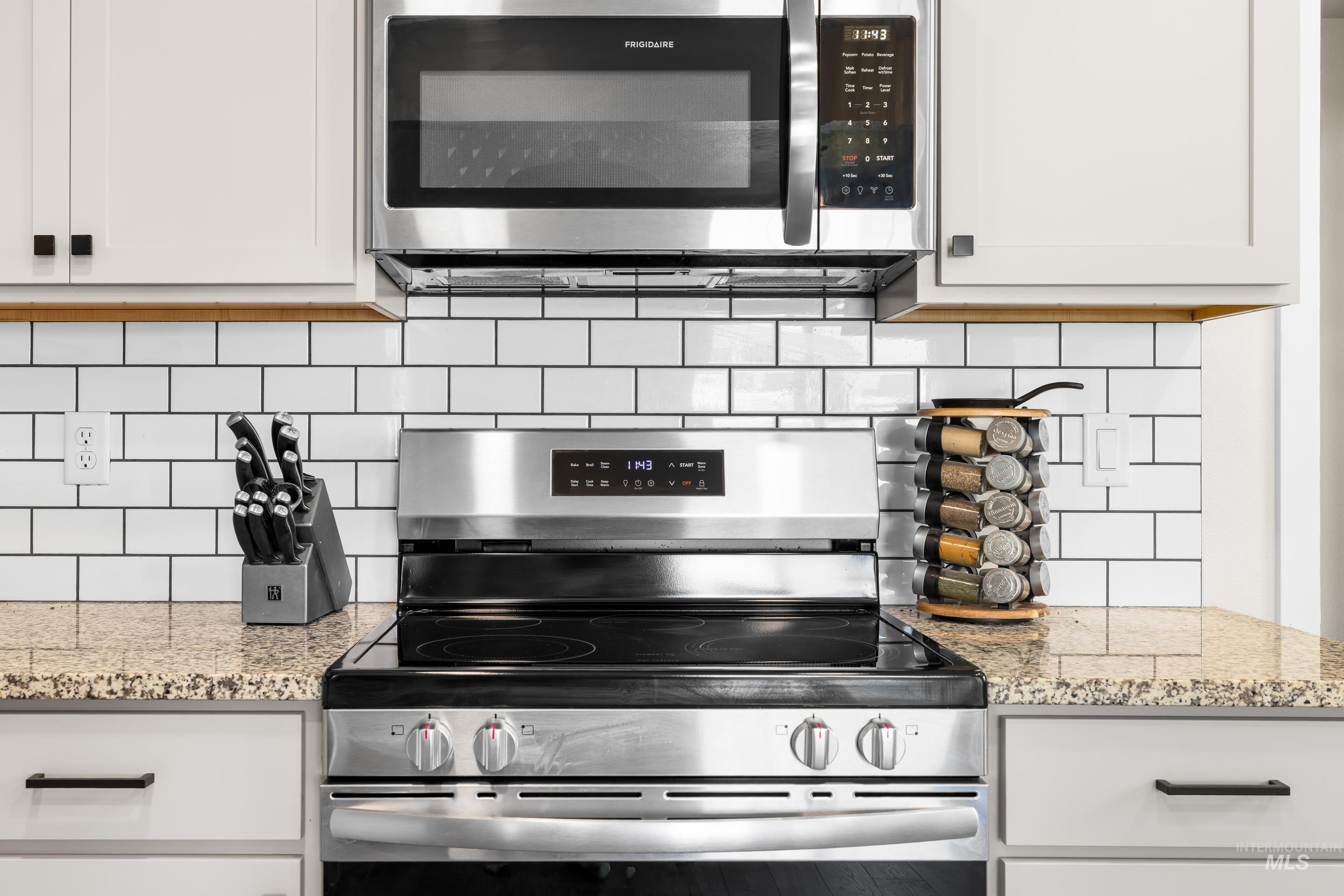 Kitchen featuring stainless steel appliances, light stone counters, white cabinetry, and decorative backsplash