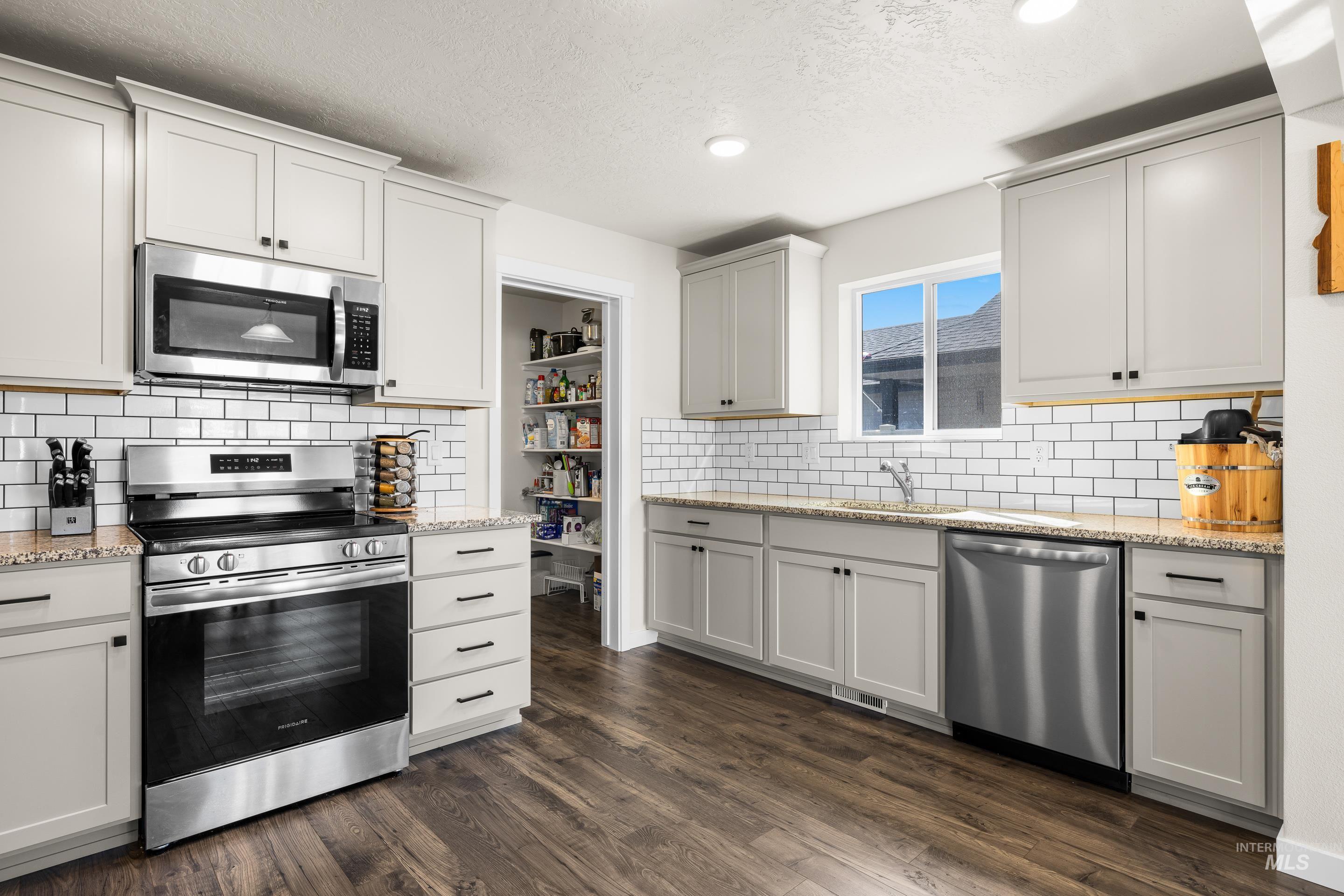 Kitchen with appliances with stainless steel finishes, light stone counters, tasteful backsplash, dark wood finished floors, and a textured ceiling