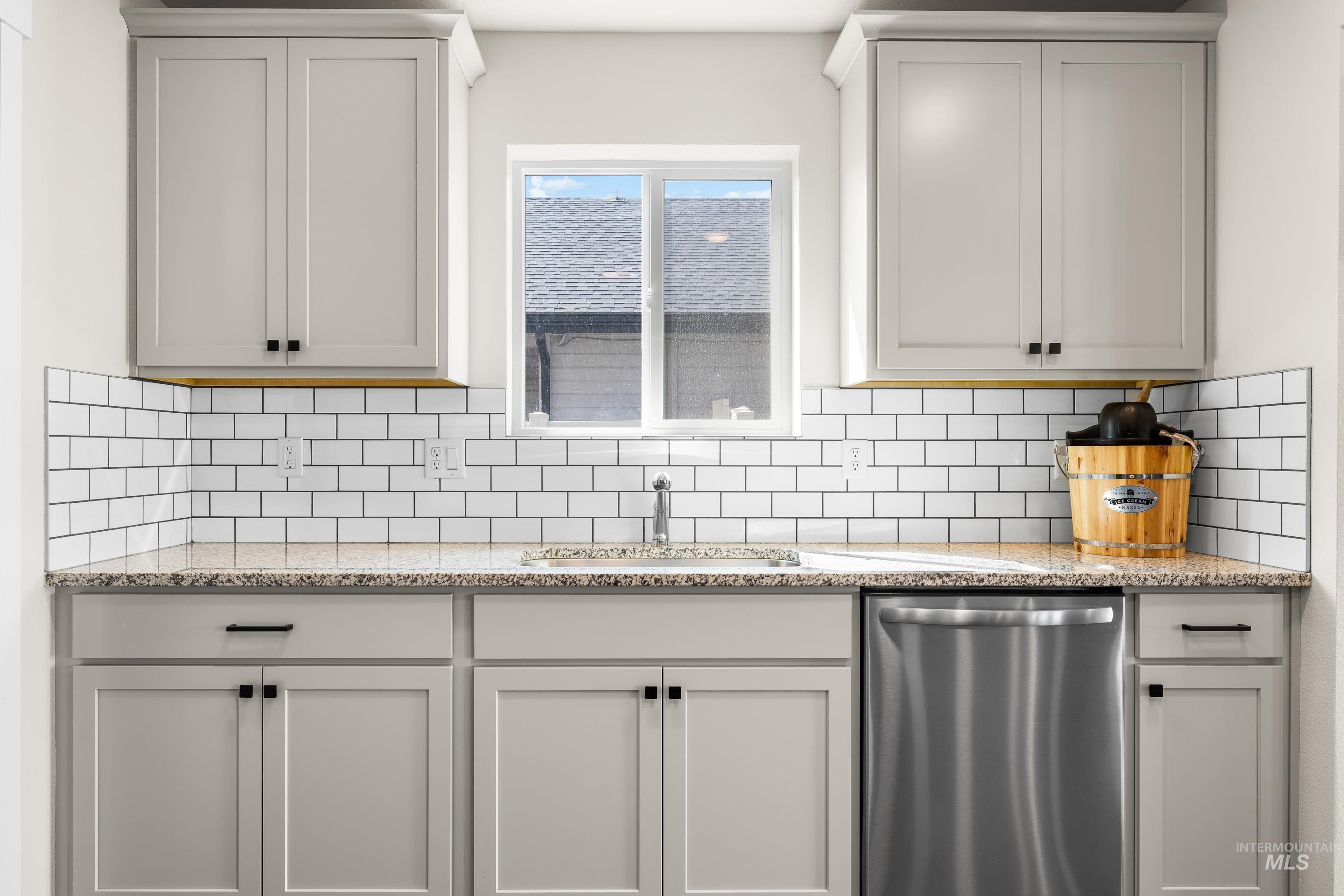 Kitchen with light stone countertops, stainless steel dishwasher, tasteful backsplash, and gray cabinets