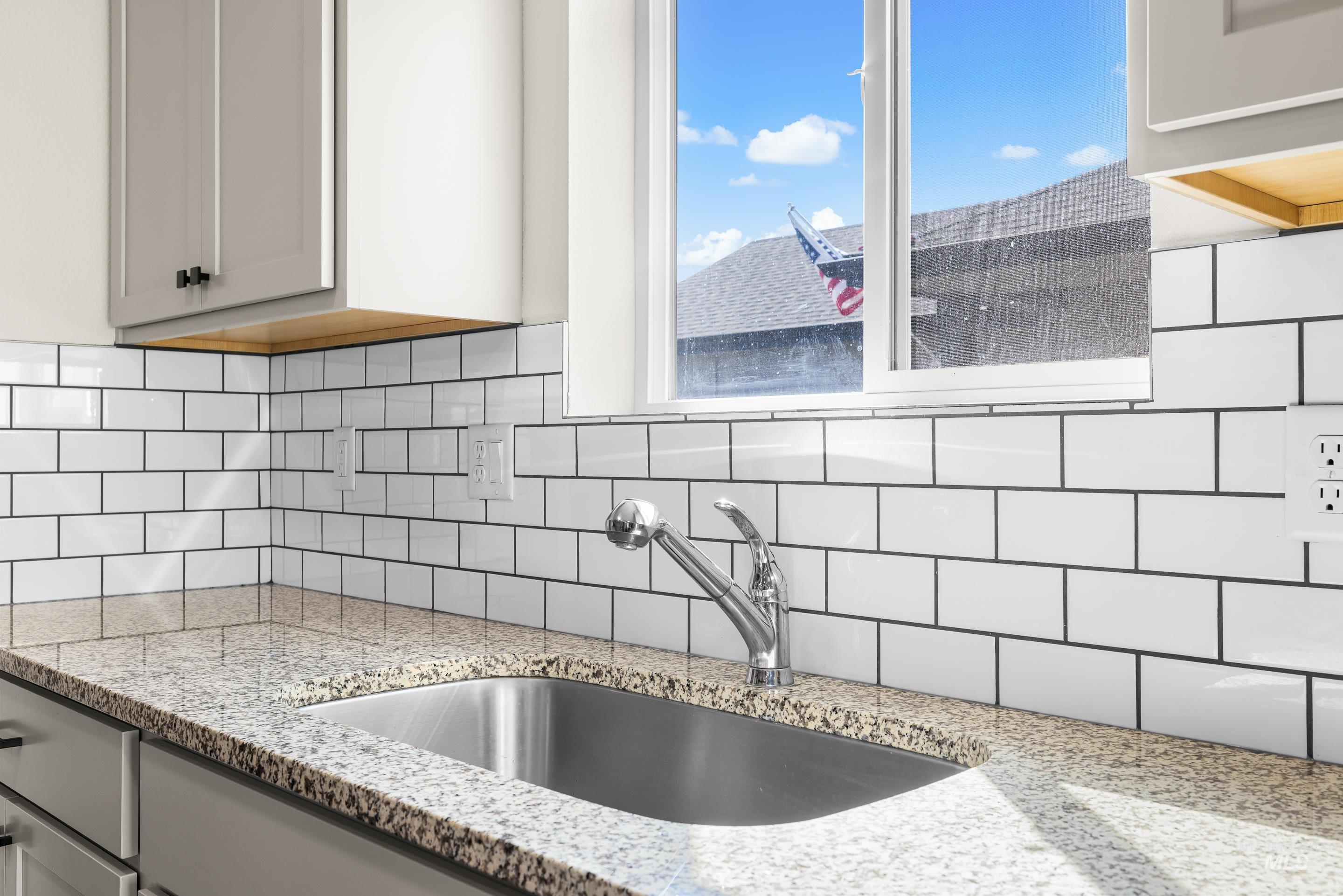 Kitchen featuring light stone counters, decorative backsplash, and gray cabinets