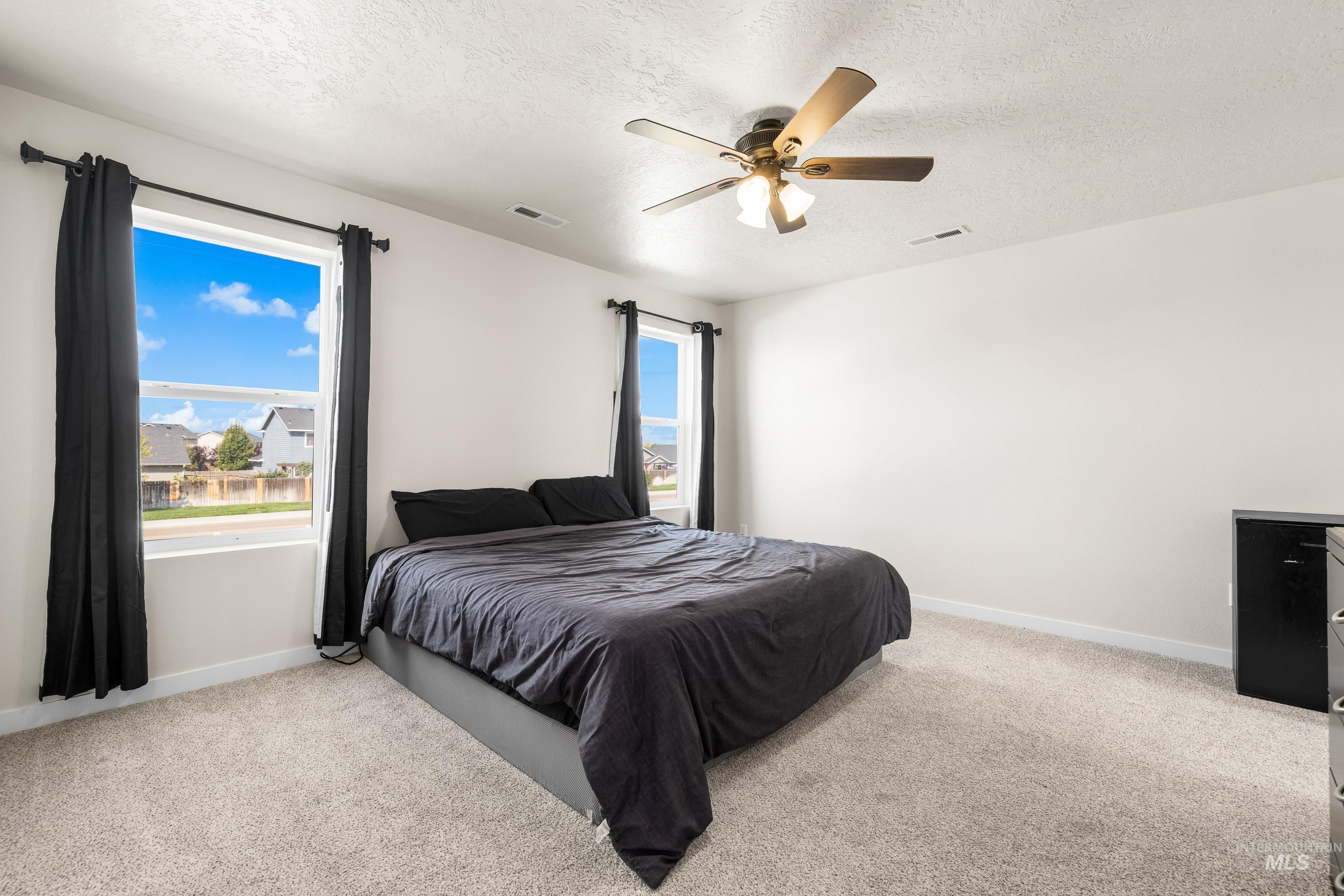 Bedroom featuring light colored carpet, multiple windows, a textured ceiling, and a ceiling fan