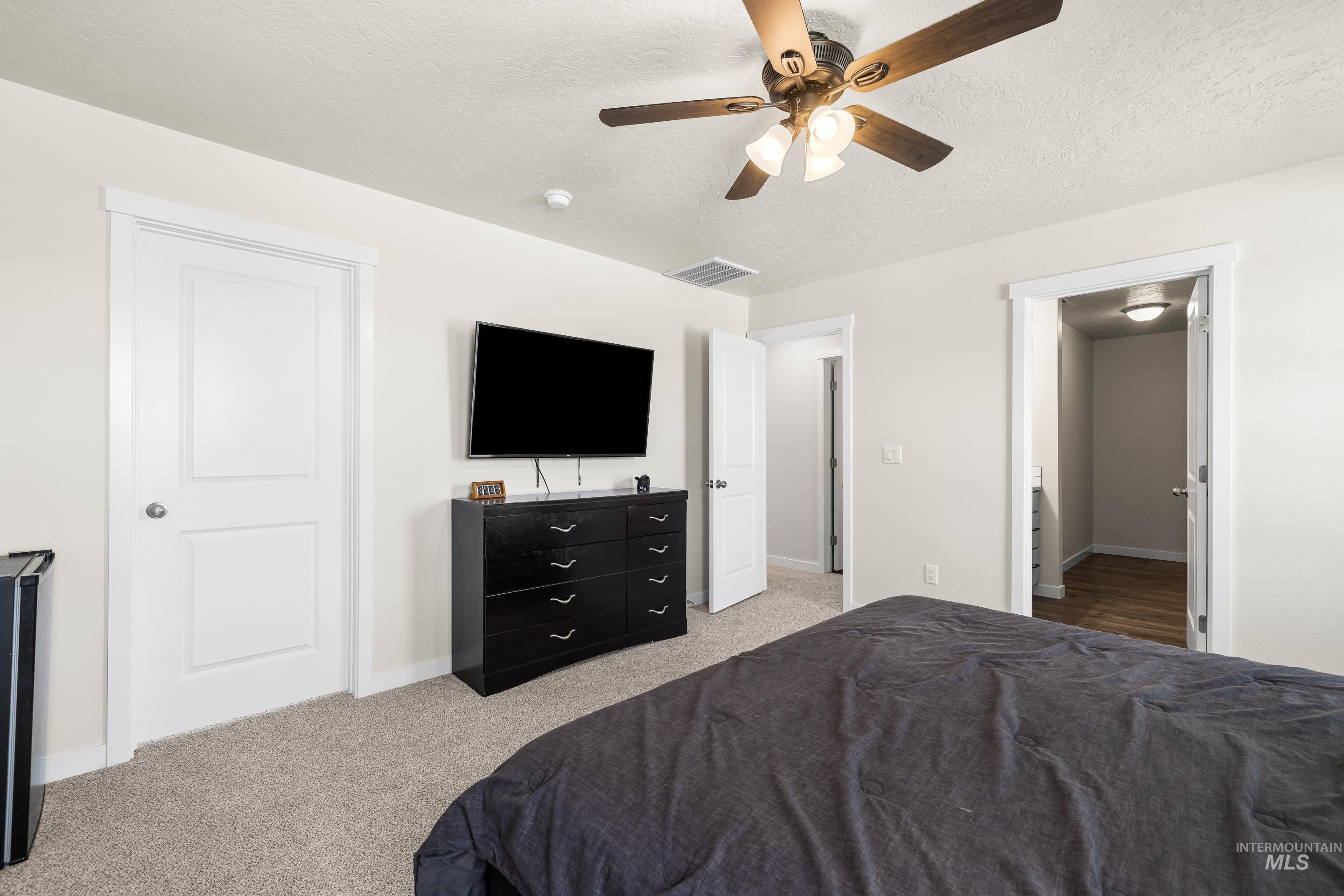 Bedroom with light carpet, a ceiling fan, and a textured ceiling