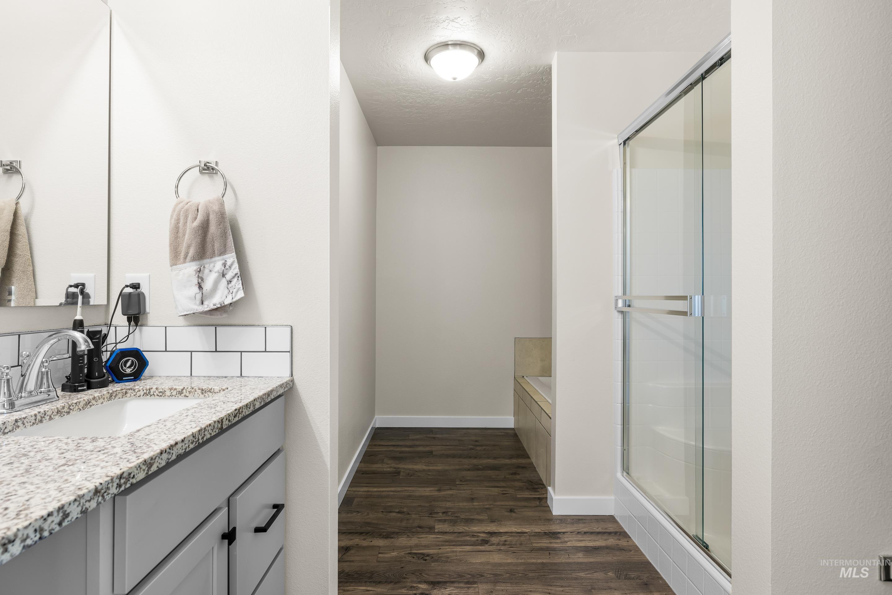 Bathroom with vanity, a textured ceiling, a stall shower, dark wood finished floors, and a garden tub