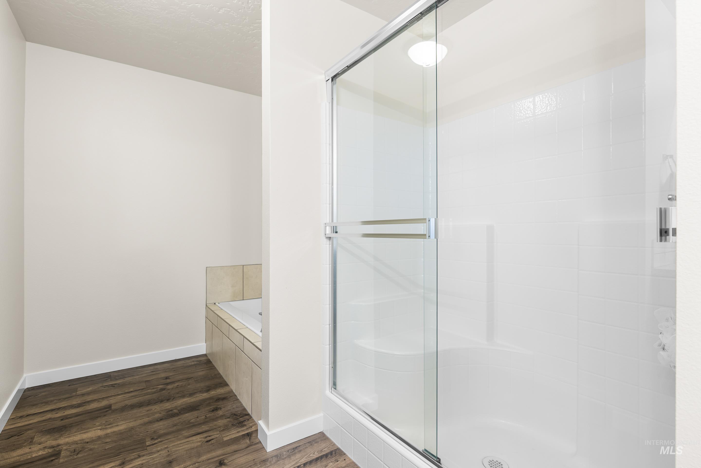 Bathroom featuring dark wood-type flooring, a shower stall, a garden tub, and a textured ceiling