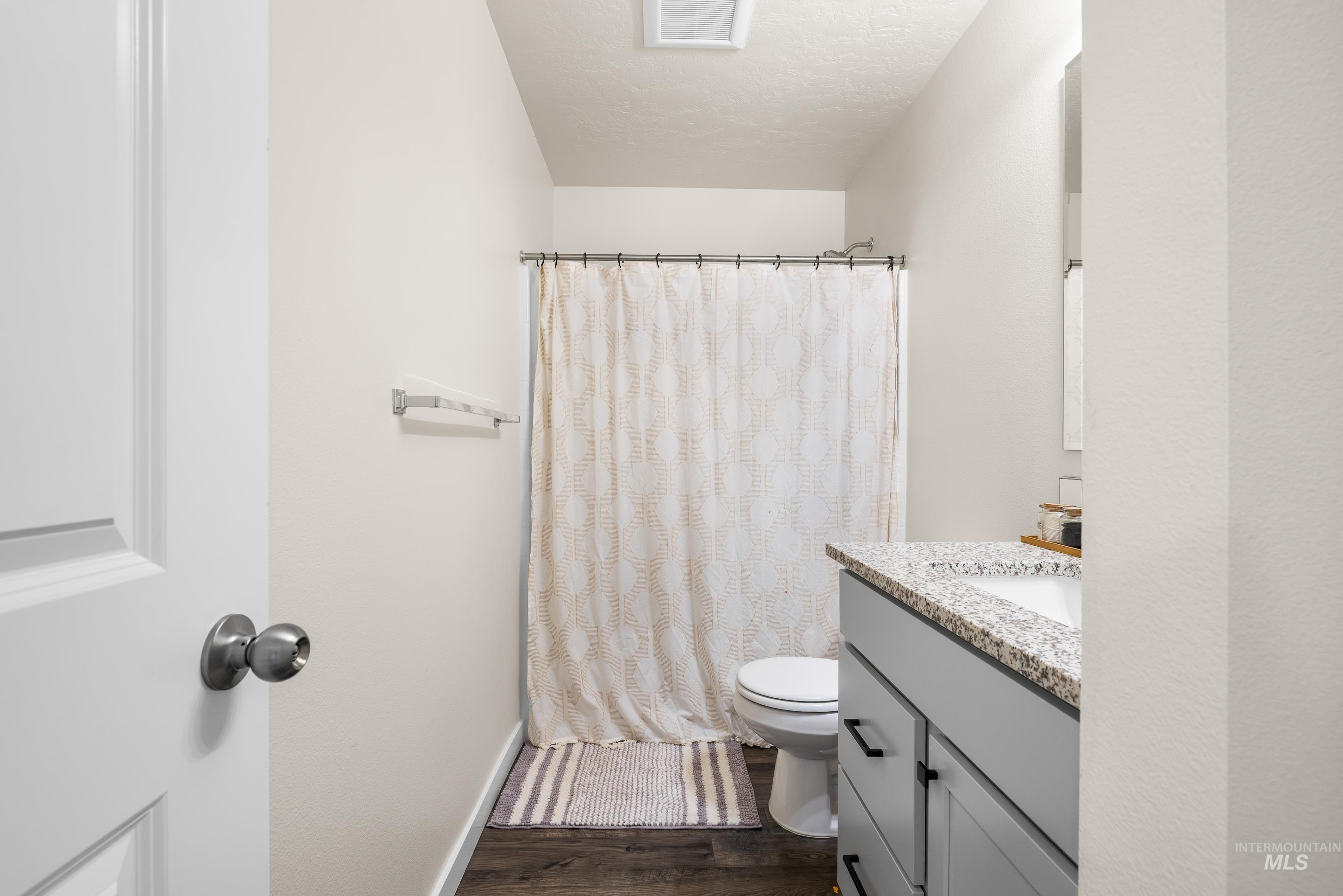 Full bathroom featuring vanity, dark wood-type flooring, a shower with curtain, and a textured ceiling