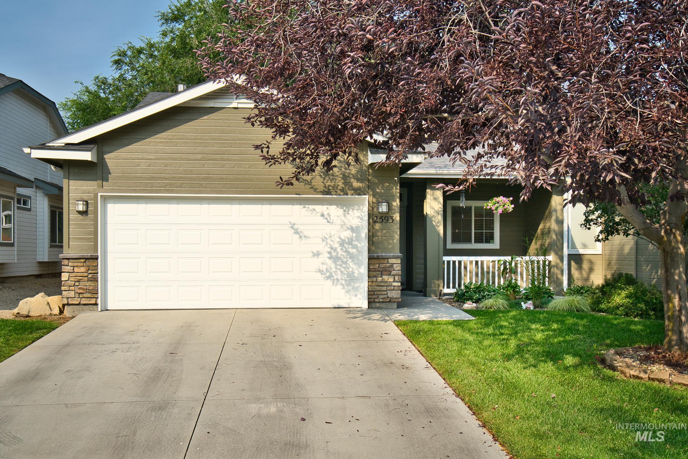 View of front of house with stone siding, driveway, an attached garage, a front lawn, and a porch