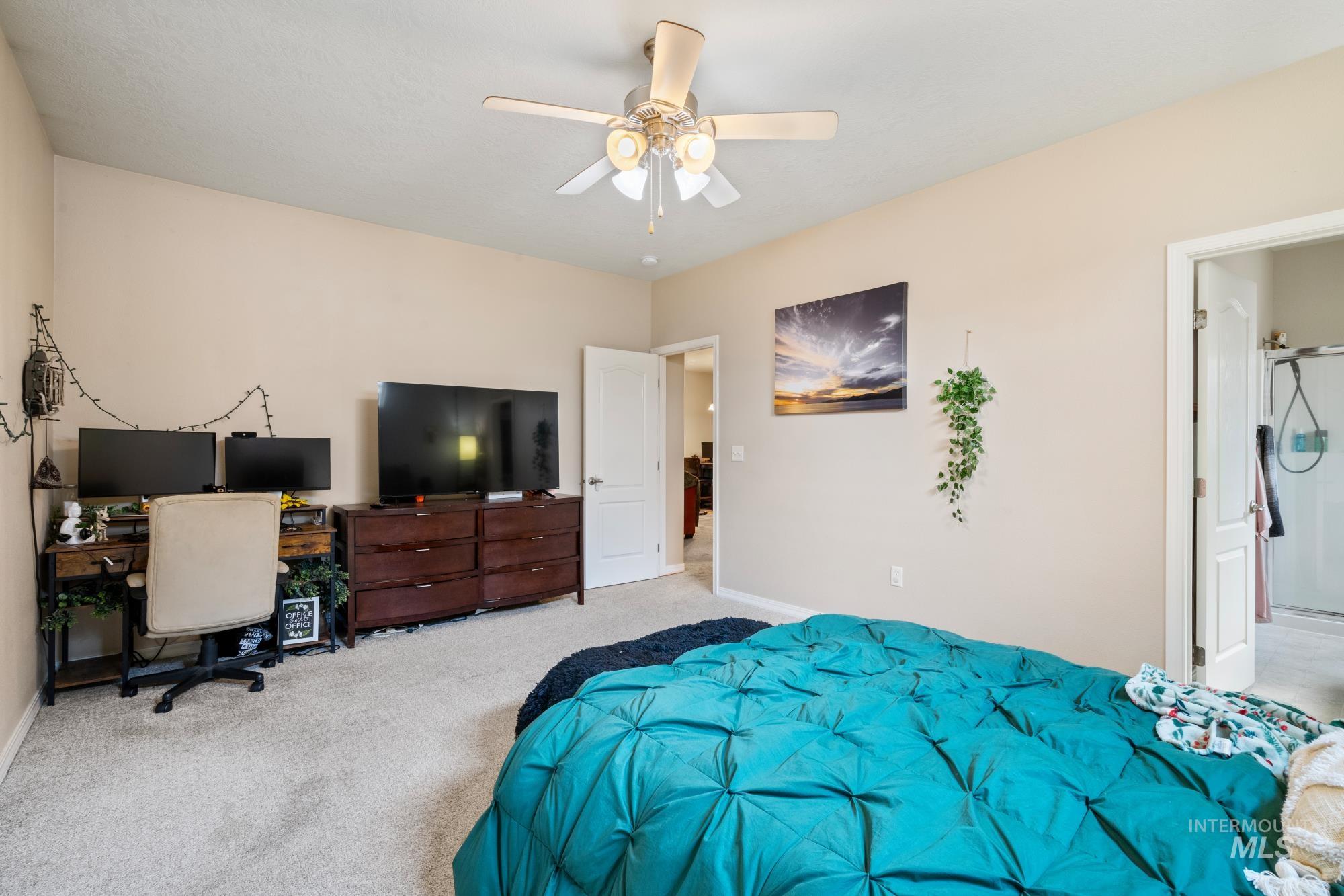 Carpeted bedroom with an office area, ceiling fan, and ensuite bathroom
