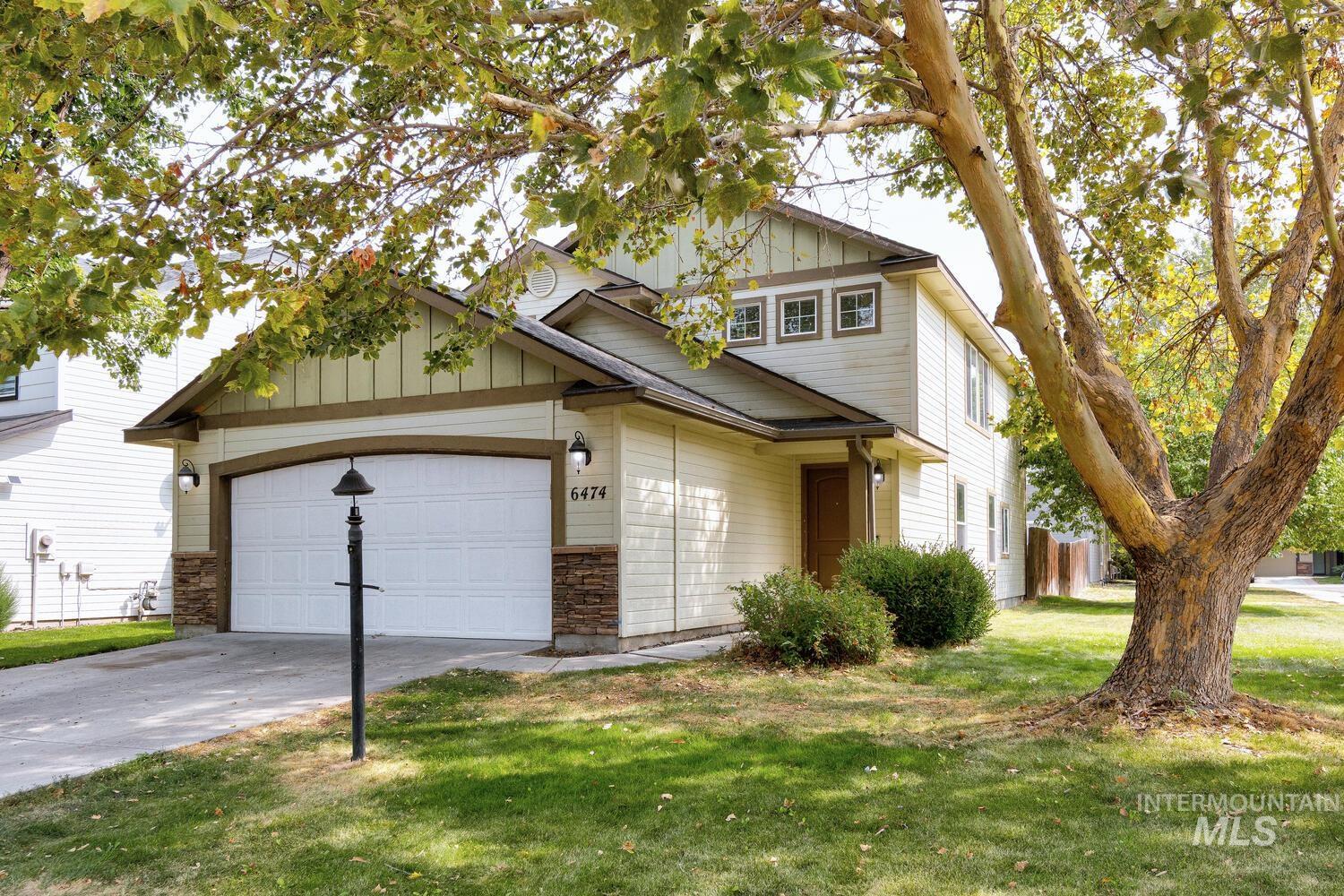 View of front of property featuring board and batten siding, a front yard, driveway, a garage, and stone siding