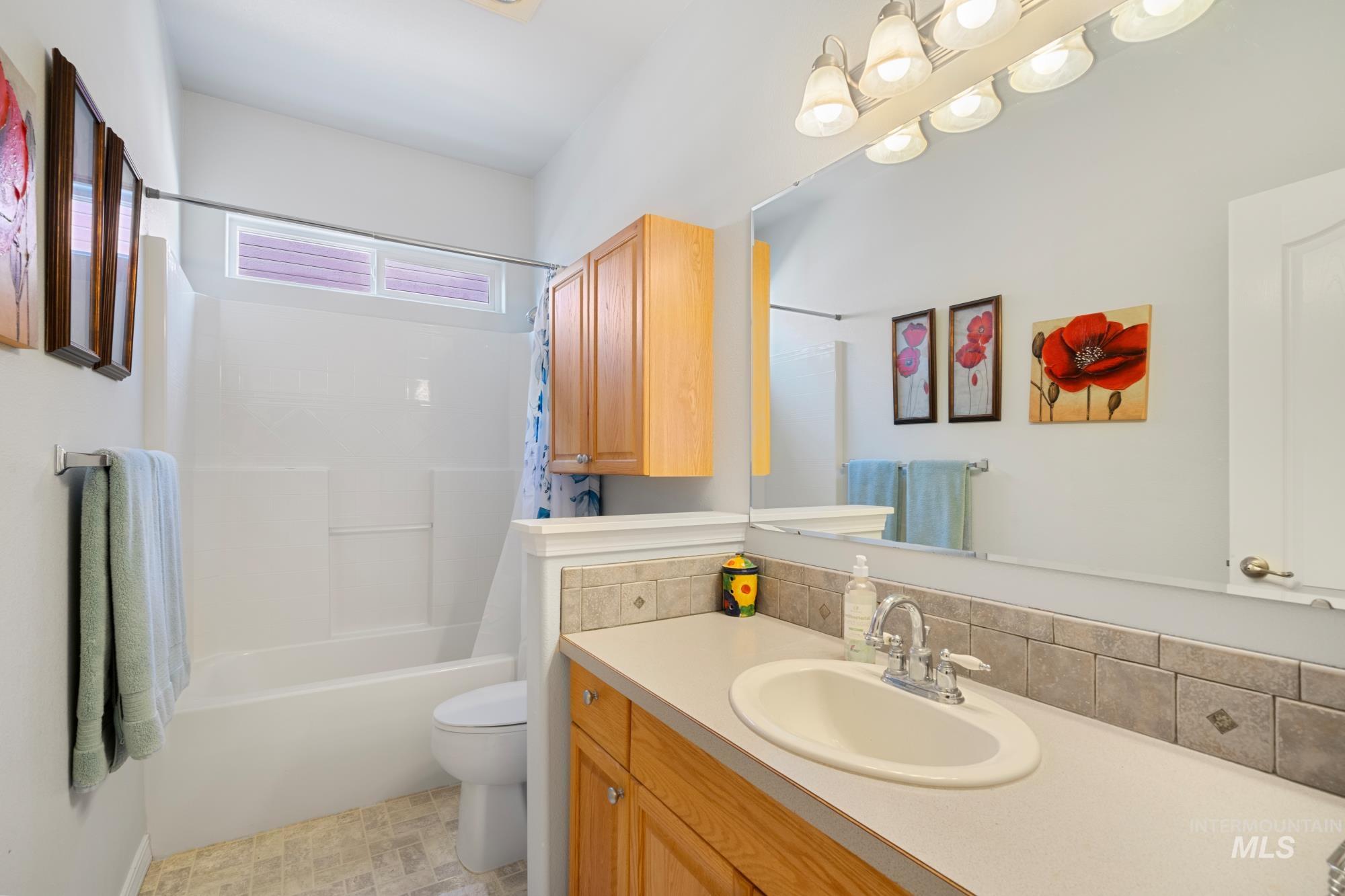 Bathroom featuring shower / bathtub combination with curtain, vanity, and backsplash