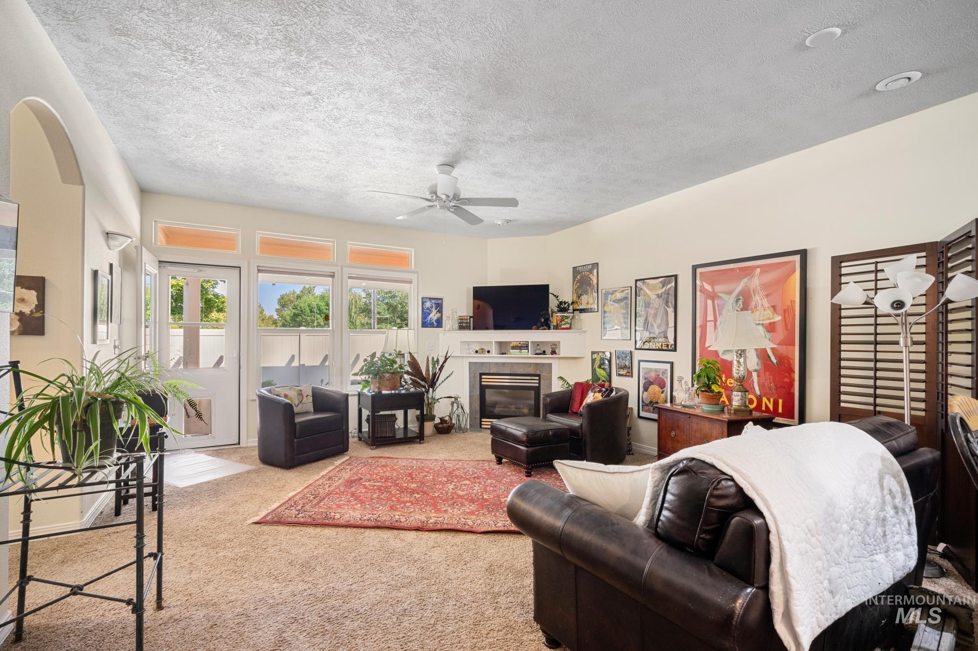 Carpeted living room featuring a textured ceiling, a tiled fireplace, and ceiling fan